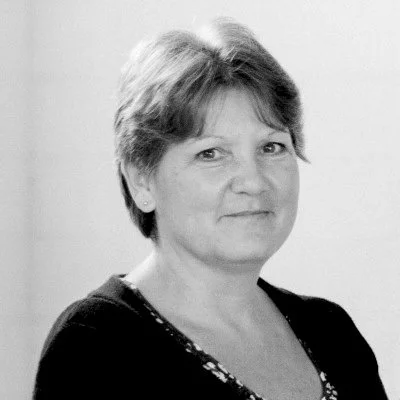 Black and white portrait of a middle-aged woman with short hair, wearing a dark top with a patterned neckline.