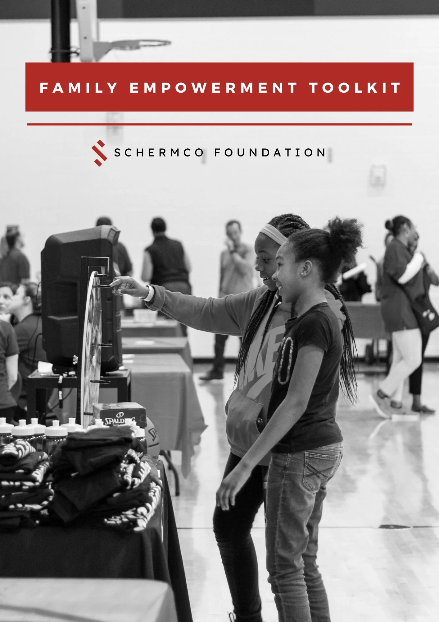 Two young girls shopping at a black-and-white community event, looking at merchandise and computer screen, with other people in the background.
