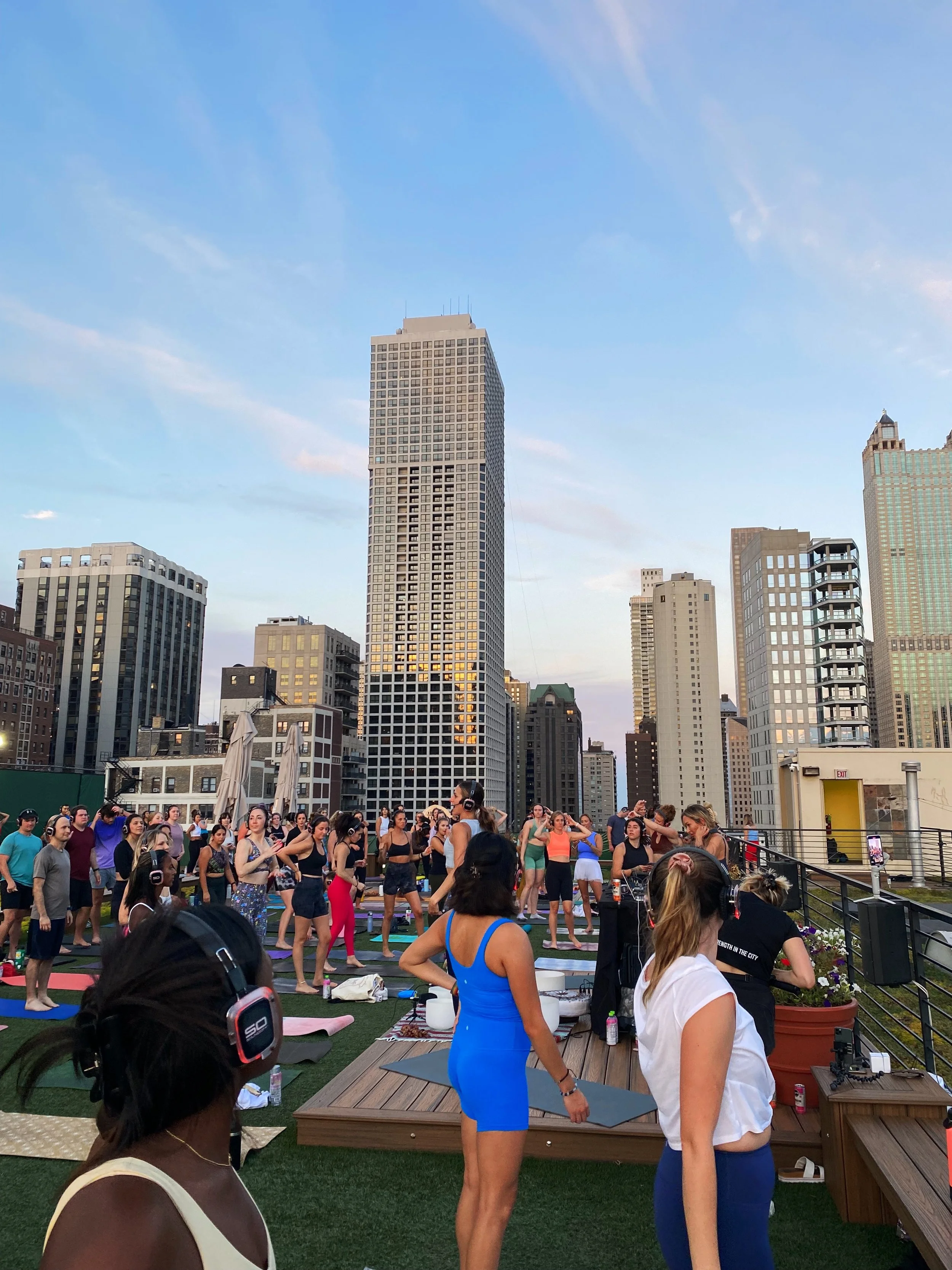 People participating in a rooftop yoga class wearing wireless headphones, with a city skyline in the background.