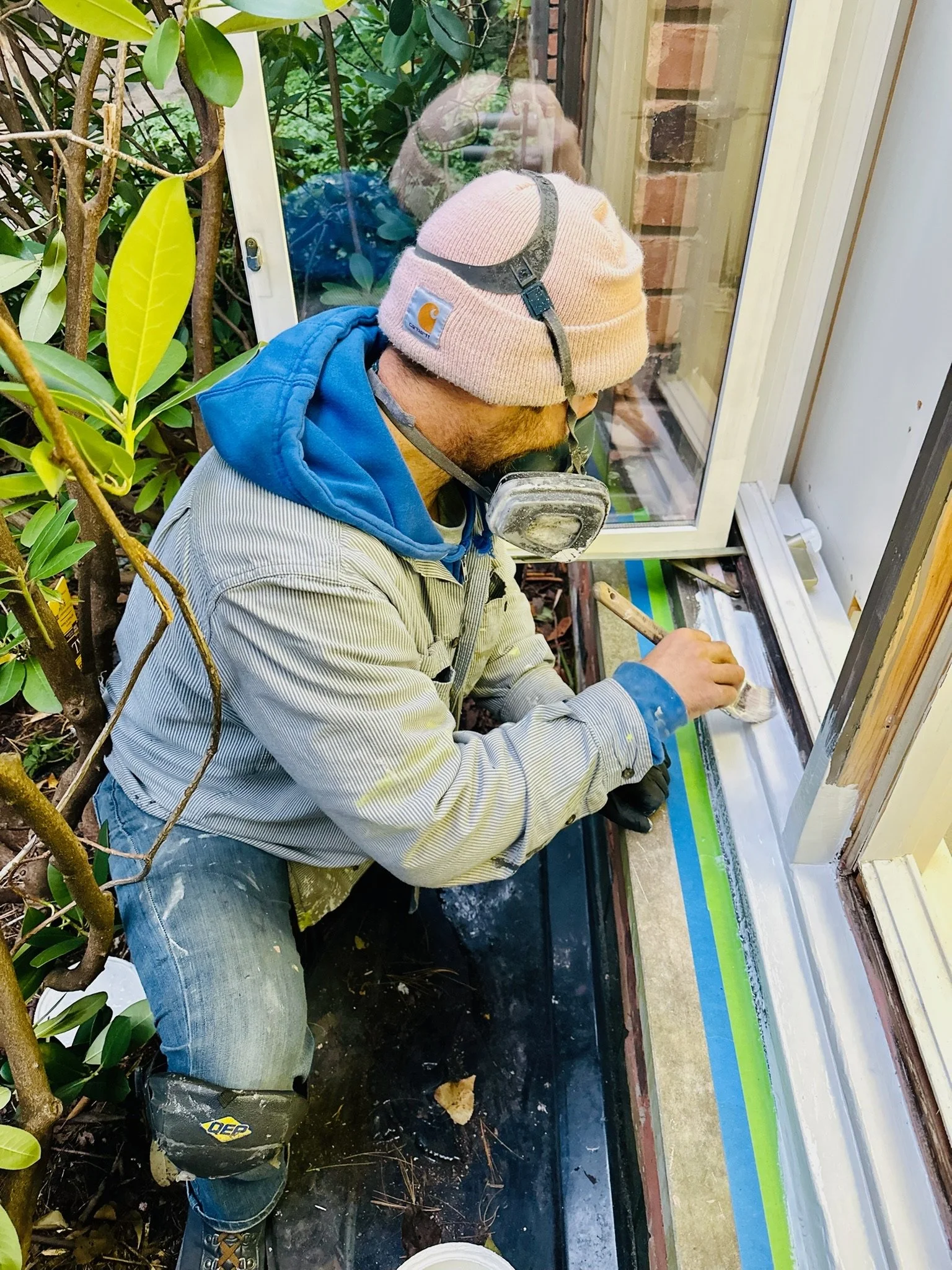 Technician wearing a respirator working on protected exterior window wood restoration
