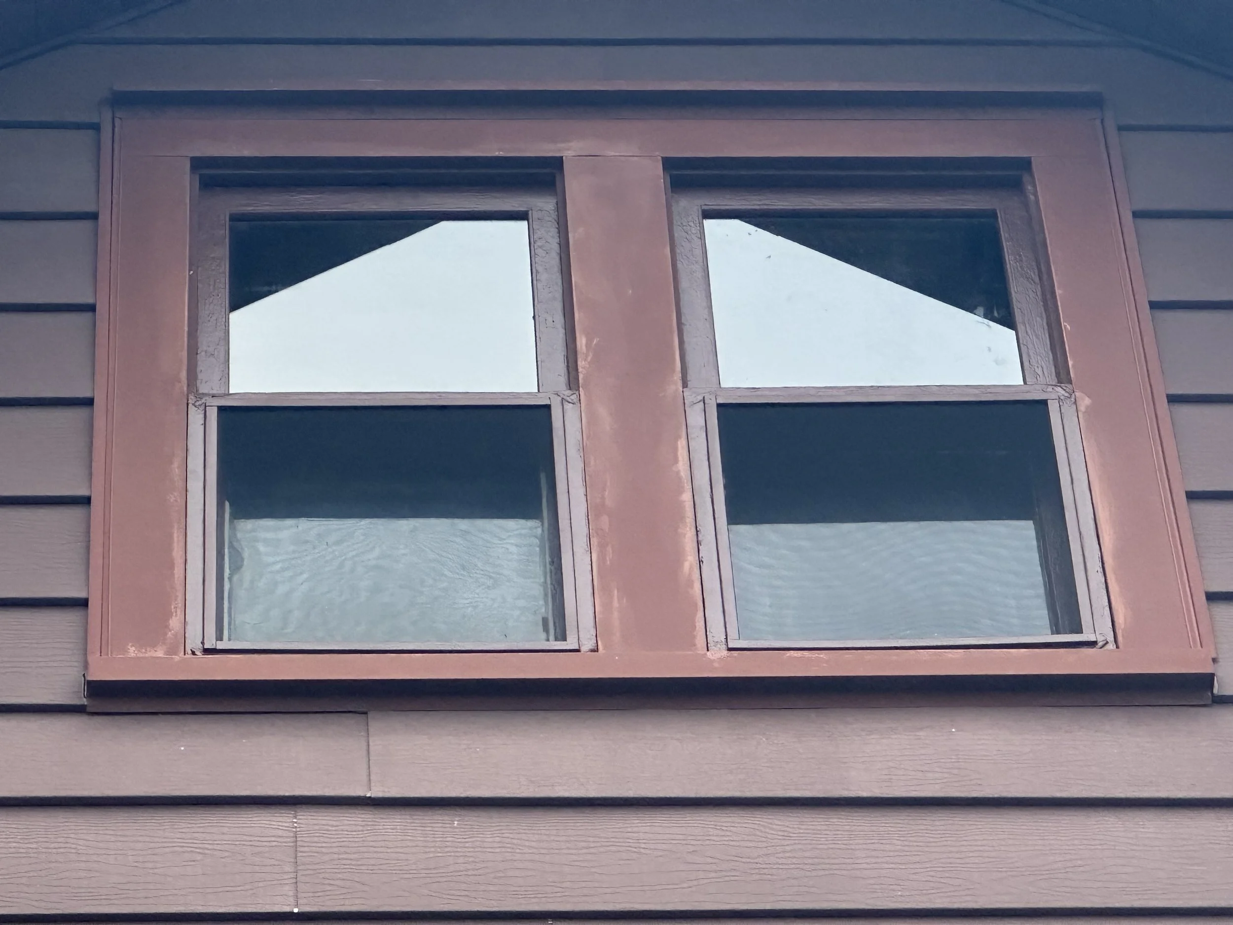 Close-up of a window with a brown frame on a house with gray horizontal siding.