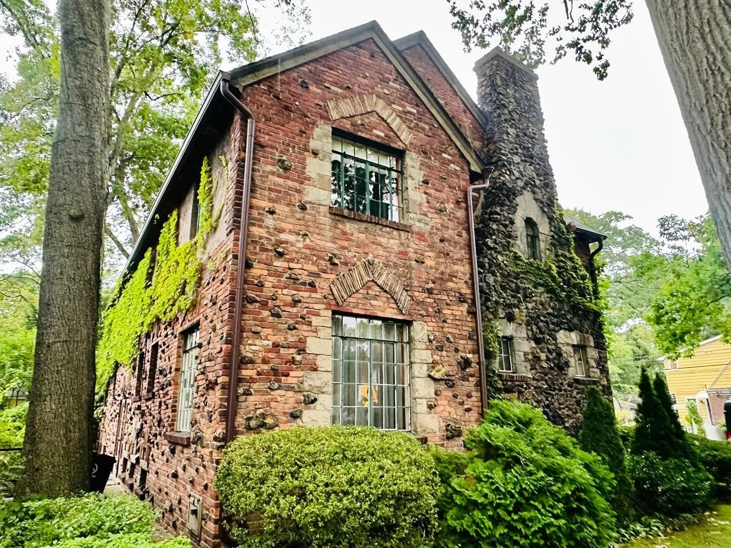 A historic brick and stone house surrounded by lush green trees and bushes.