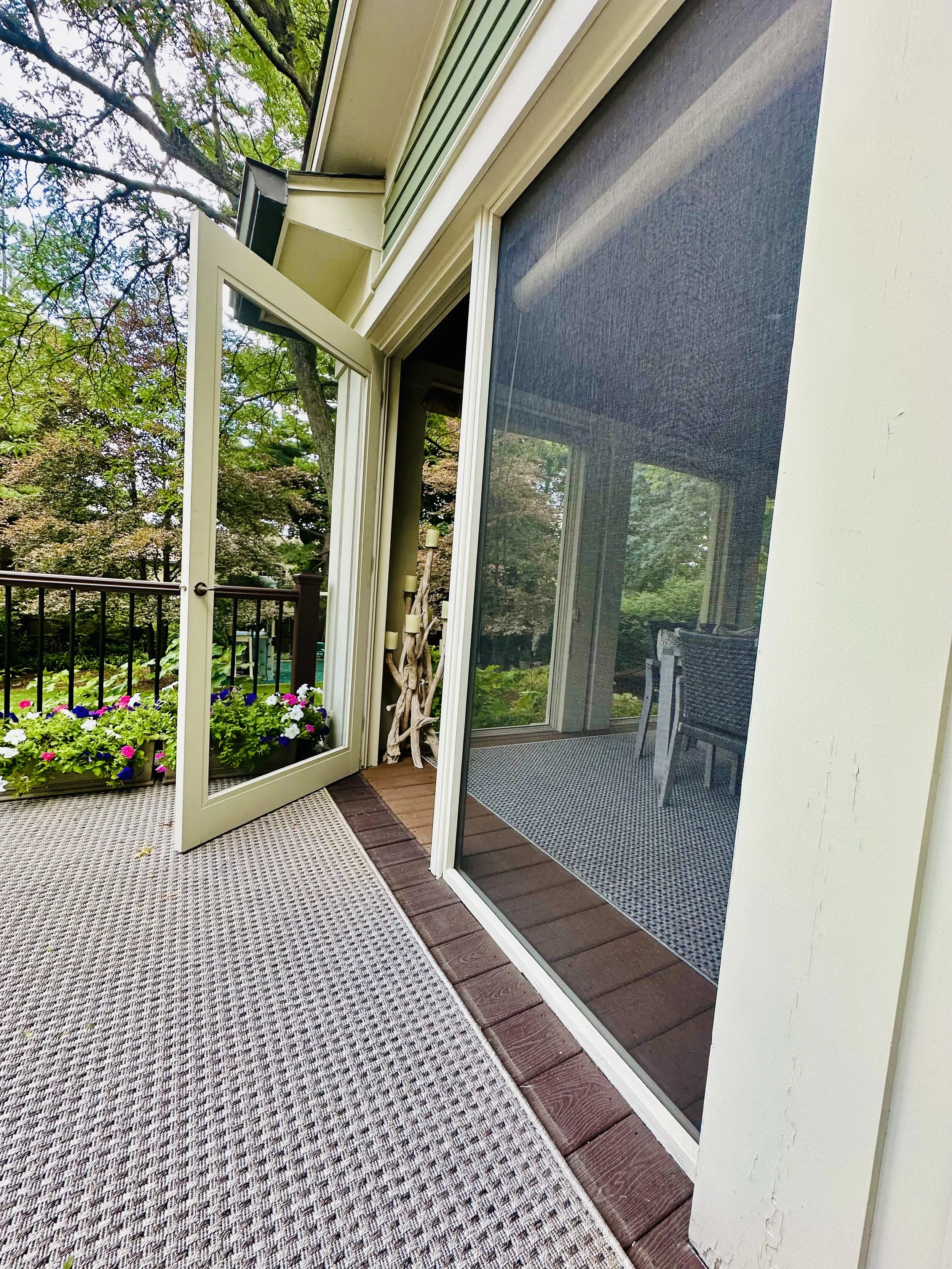 Open glass door leading to a screened-in porch with outdoor furniture and a view of trees and greenery.