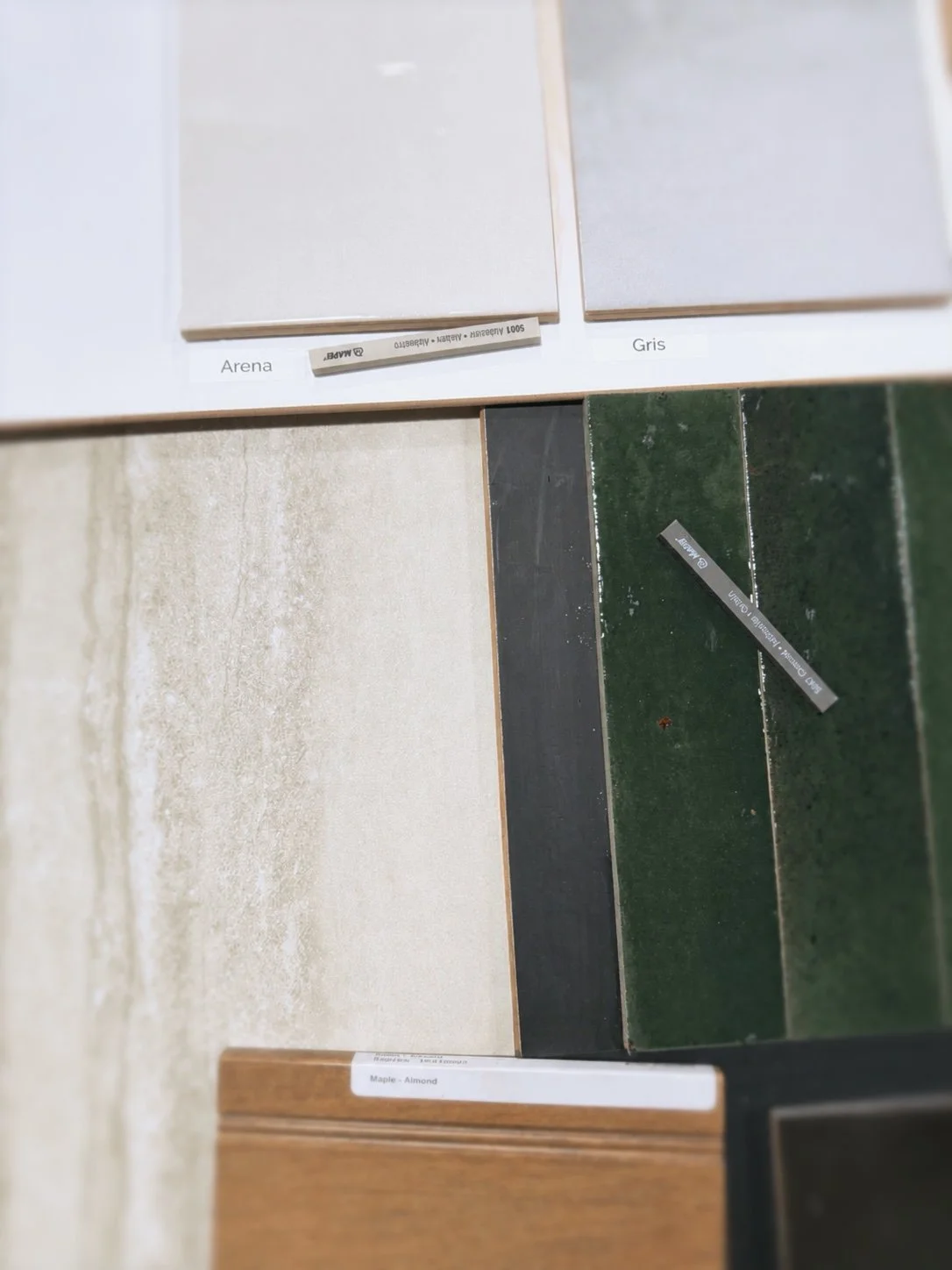 Display of various tile samples in different colors and textures, labeled with names like Arena, Gris, Maple-Almond, and others.