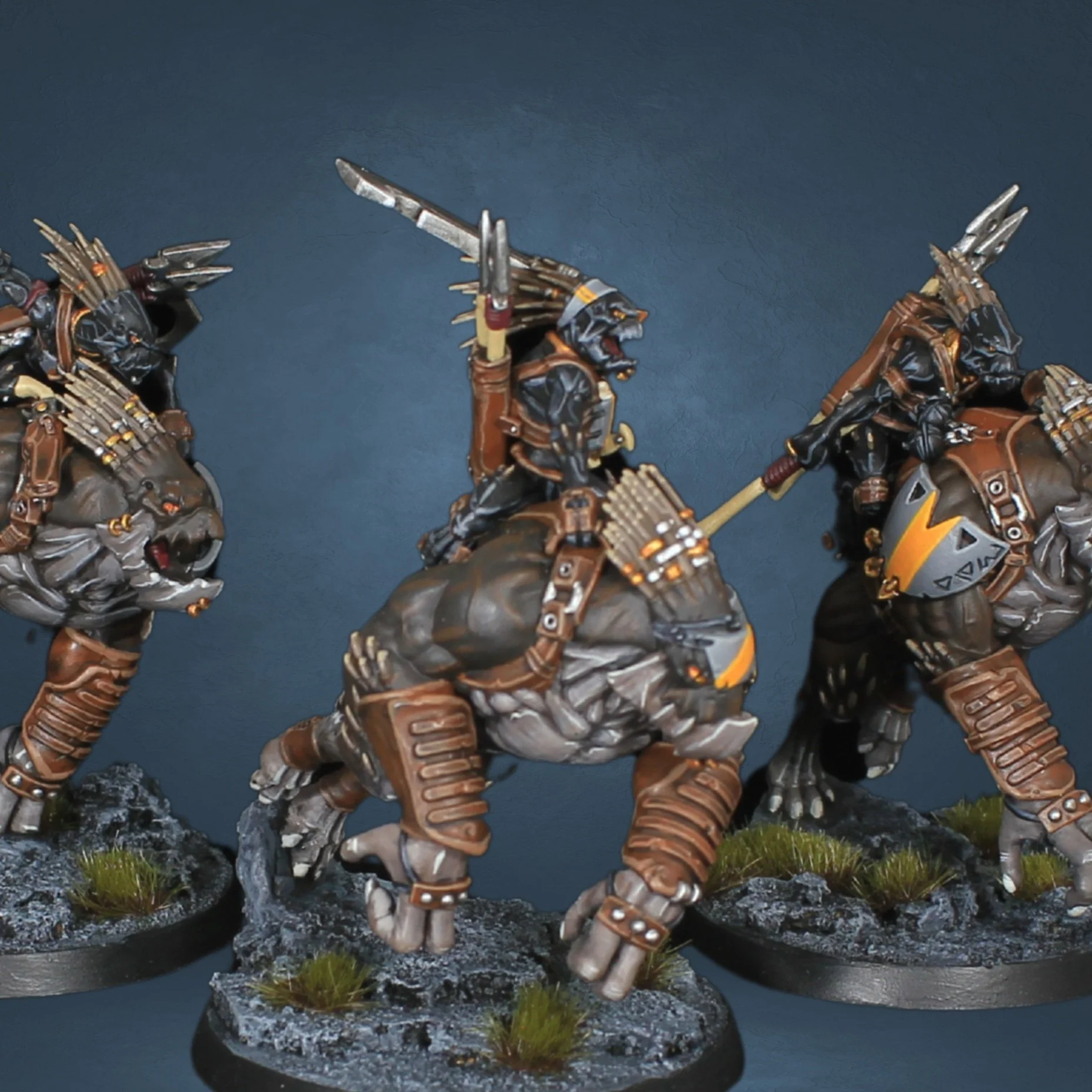 Miniature fantasy figures of armored creatures riding beast-like mounts wielding weapons, set on rocky bases with sparse grass.