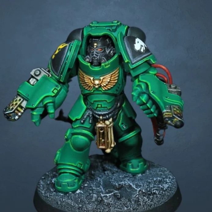 A miniature model of a green armored sci-fi soldier with a detailed helmet and weapon, standing on a textured base.