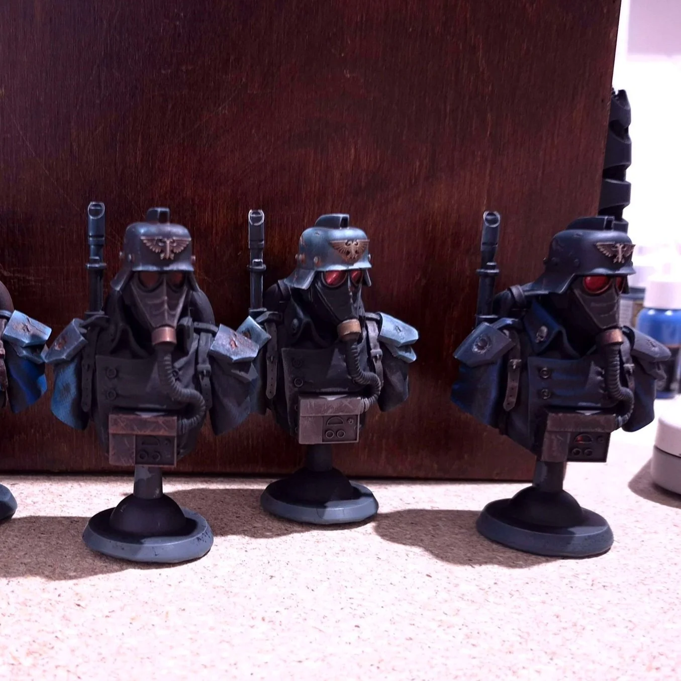 Three miniature models of sci-fi soldiers with black armor, helmets, and red visors, standing in a row on a beige surface against a brown background.