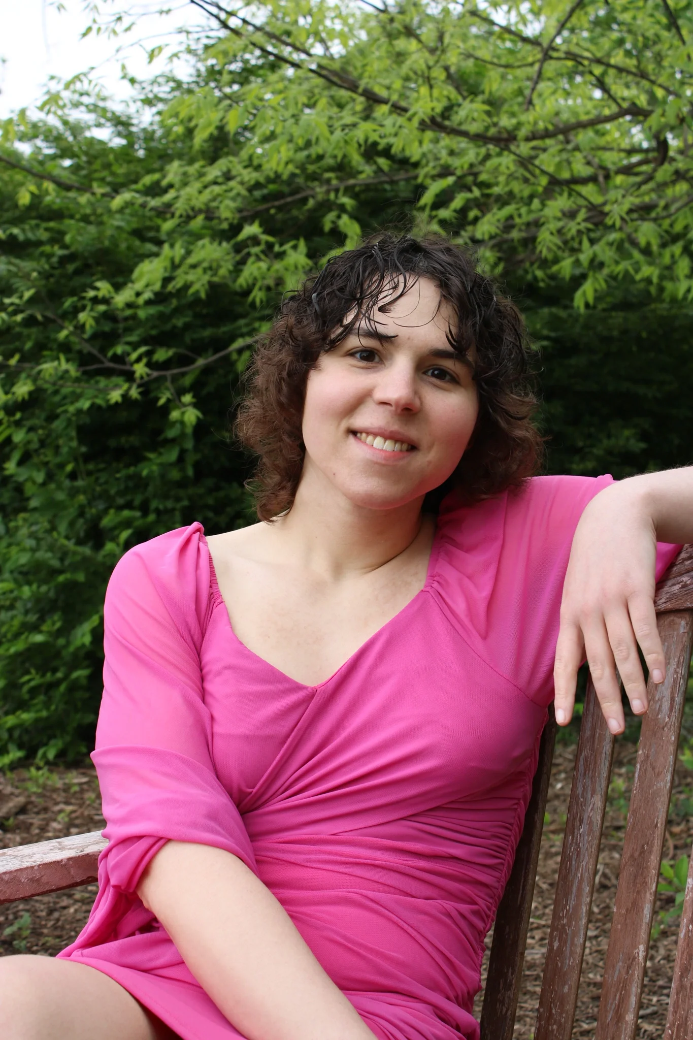 Headshot of Quin in a pink dress sitting on a park bench