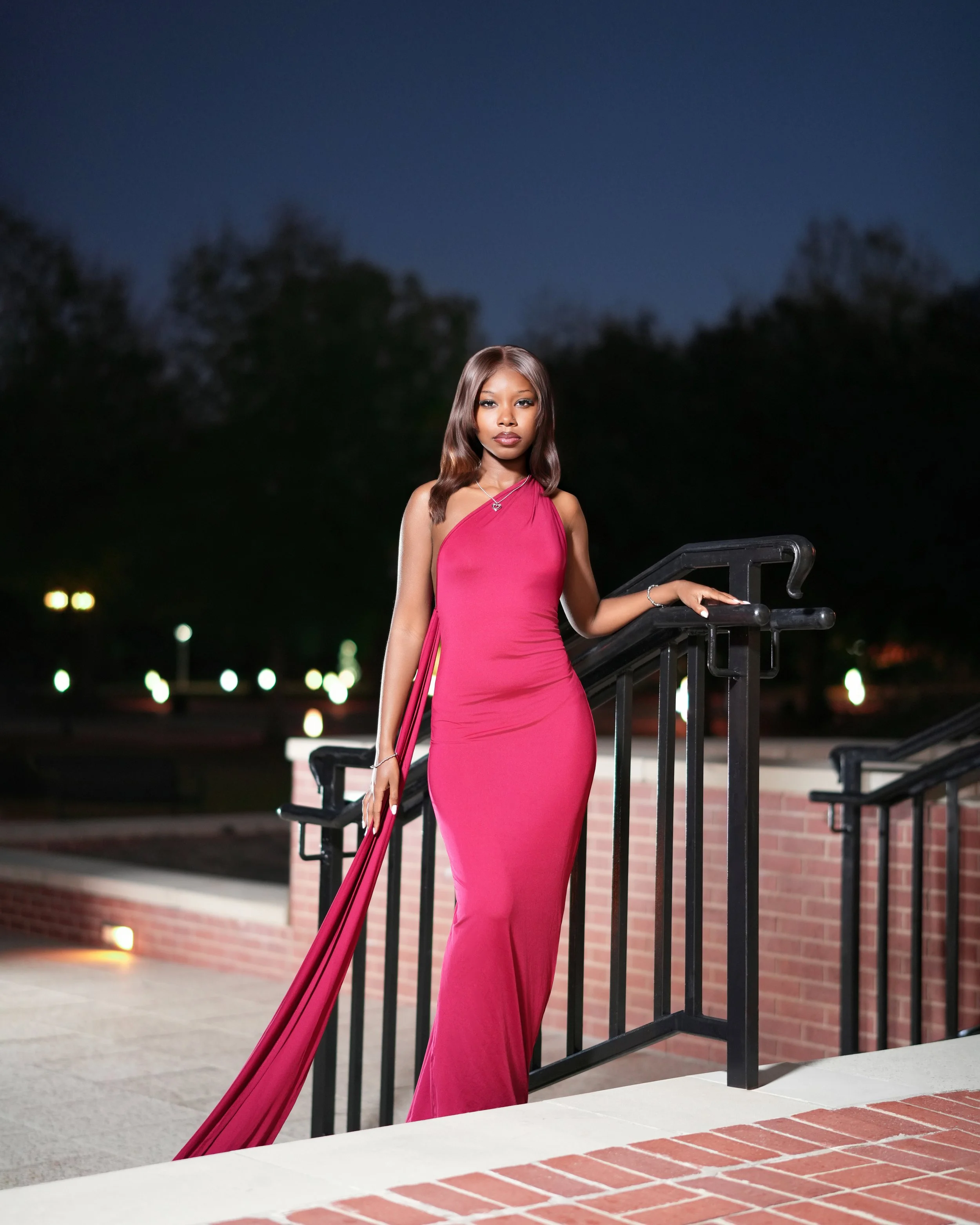 A woman in a long pink dress standing on a staircase at night.