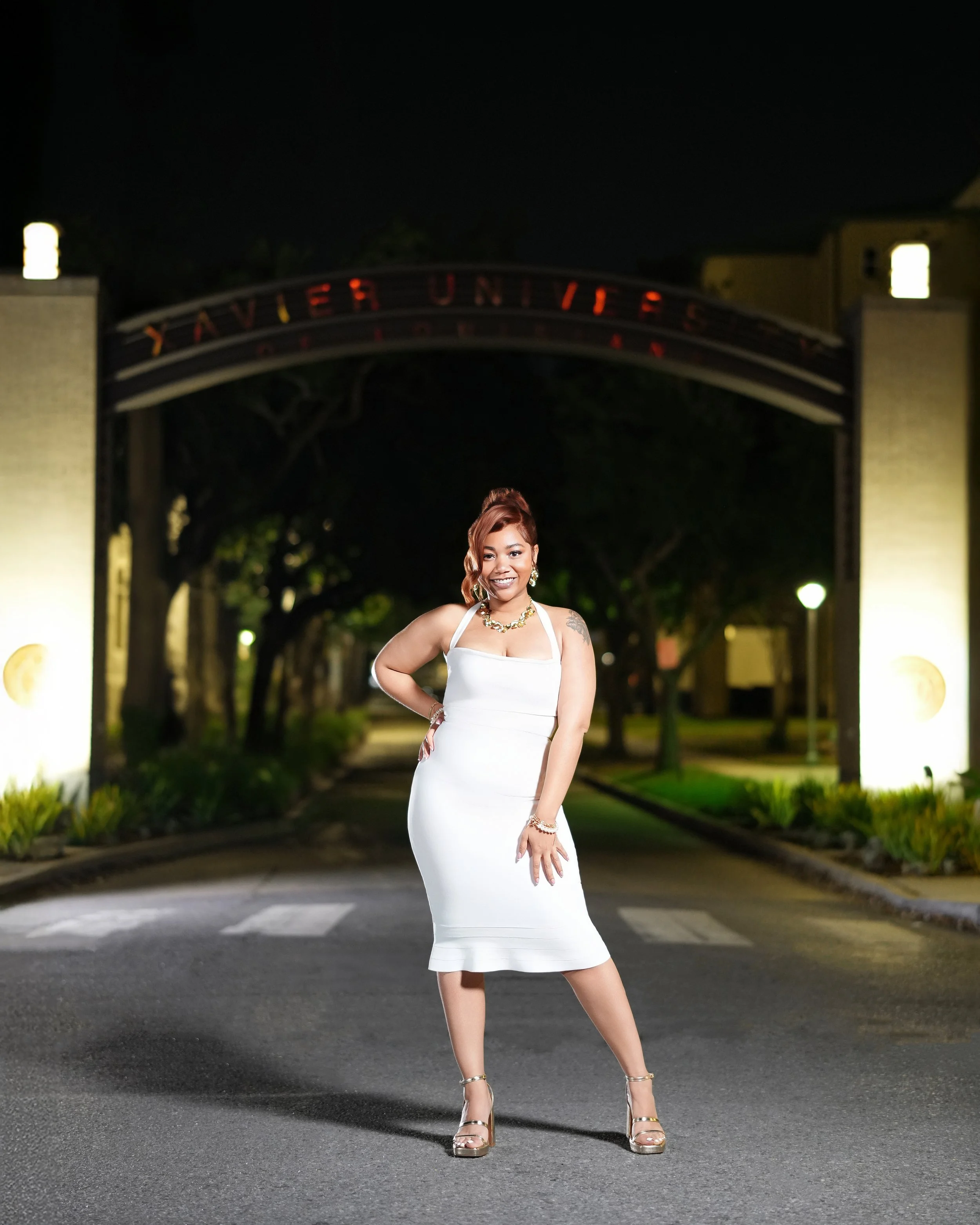 A woman in a white dress and high heels posing at night in front of the Yavapai University sign.