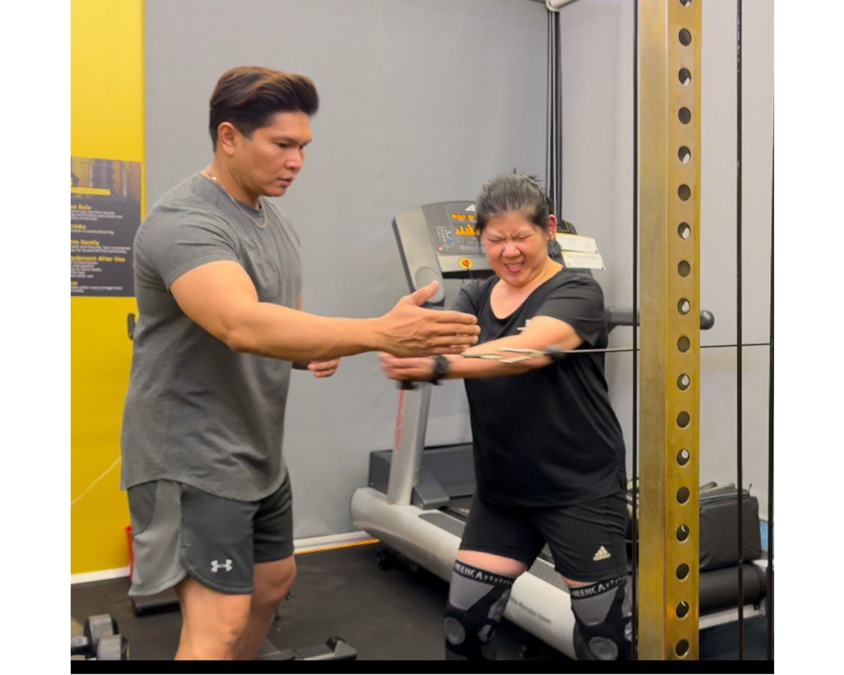 A woman exercising with cable machine assistance from a trainer in a gym.