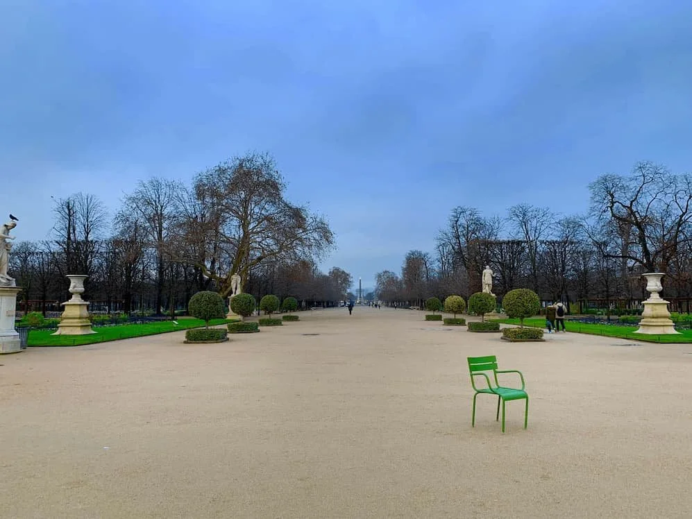 green chair in tuileries garden with trees and blue sky