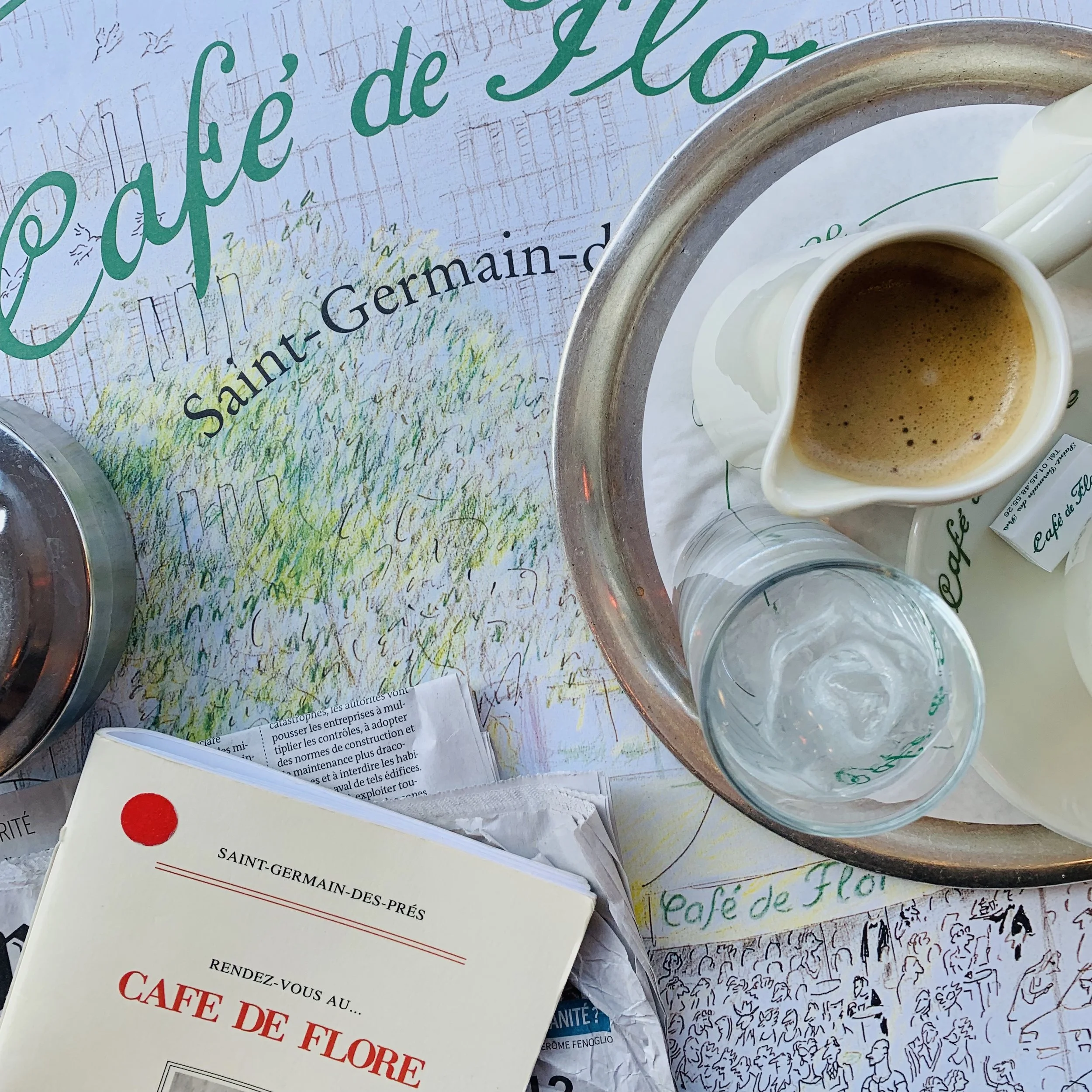 A table with various books, papers, and cups of coffee, with handwritten and printed pages scattered around  at Cafe de Flore