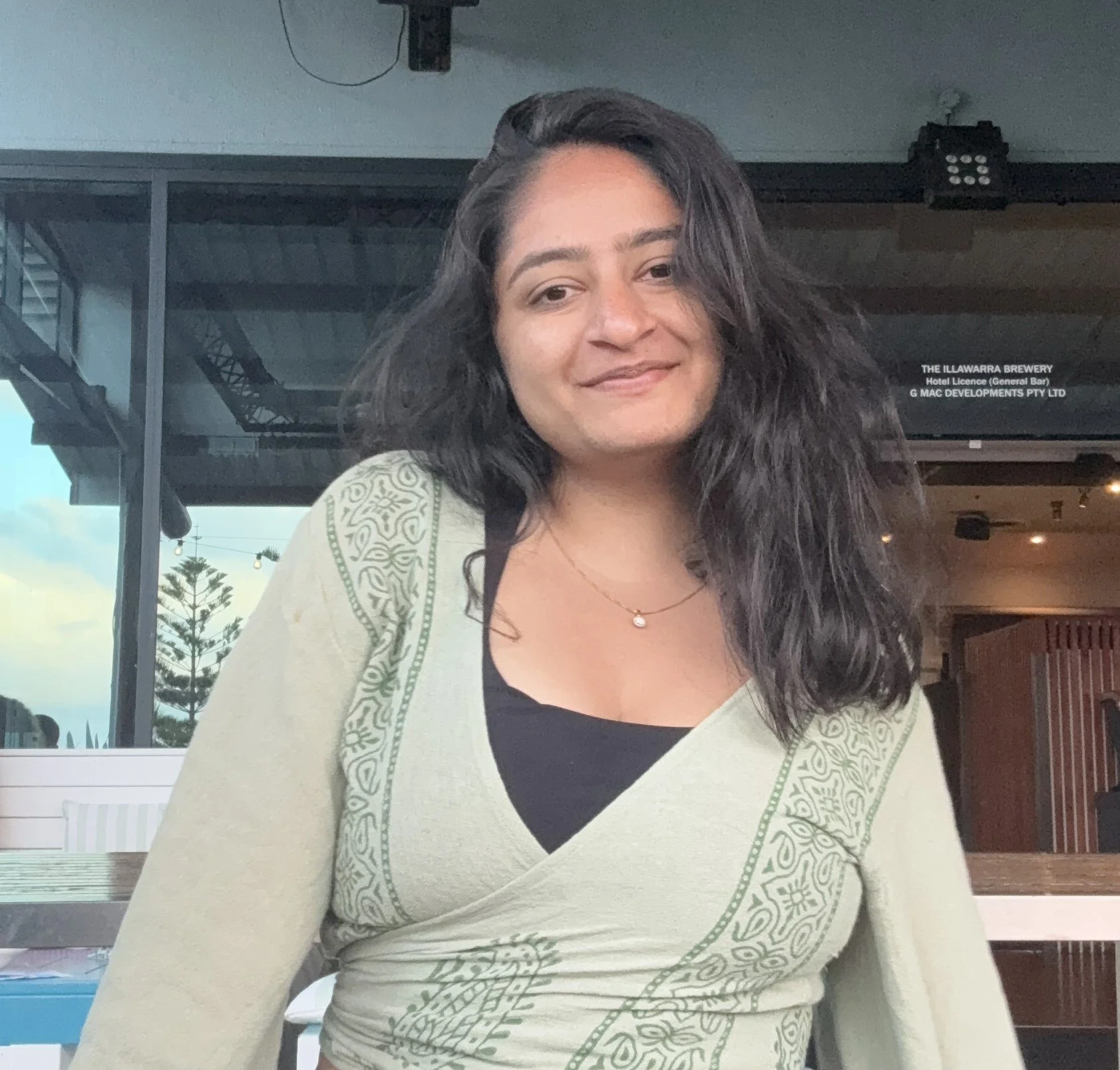 Woman with long dark hair wearing a patterned green wrap top.