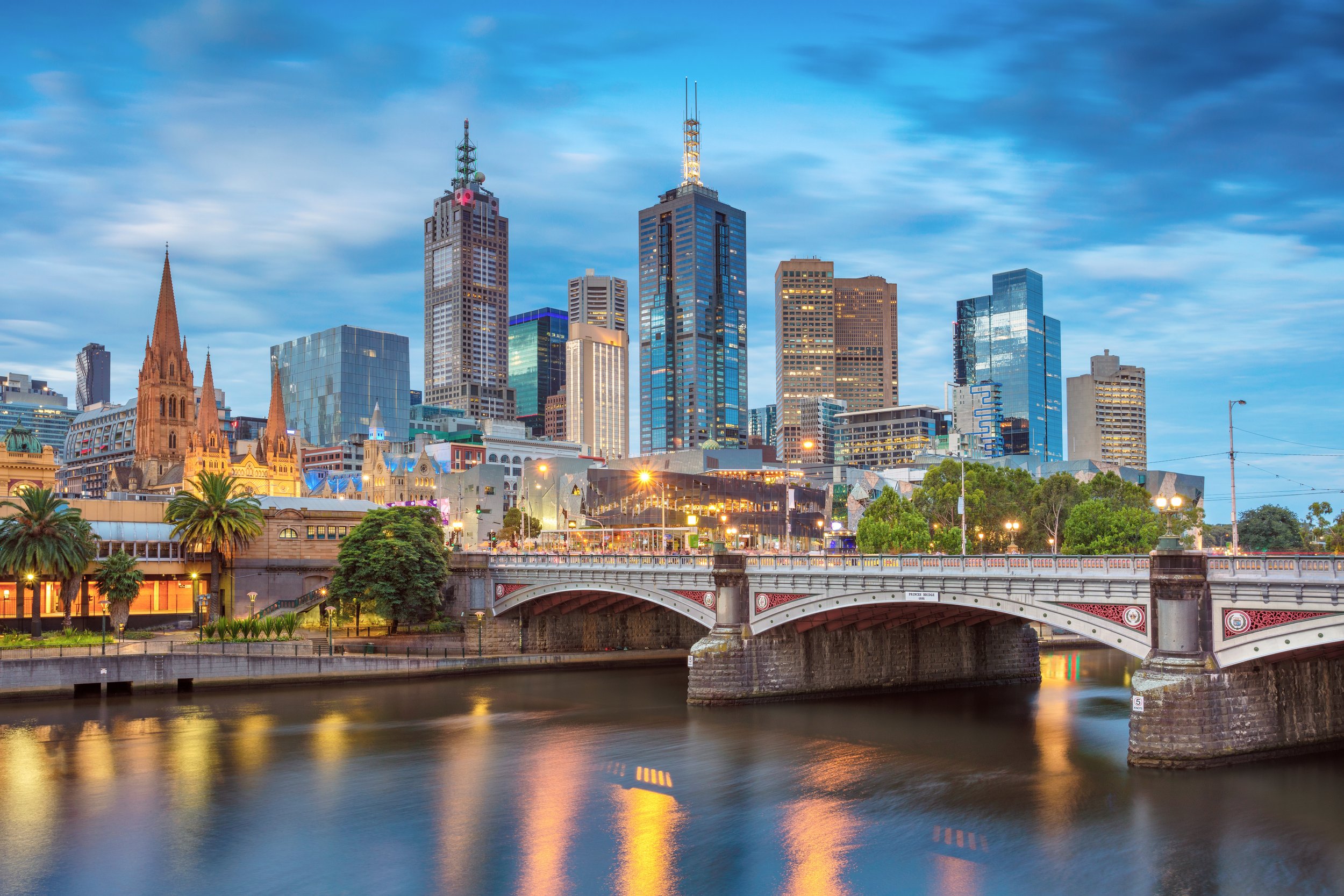 Nighttime view of downtown Melbourne, Australia with a river in the foreground and tall skyscrapers illuminated in the background.