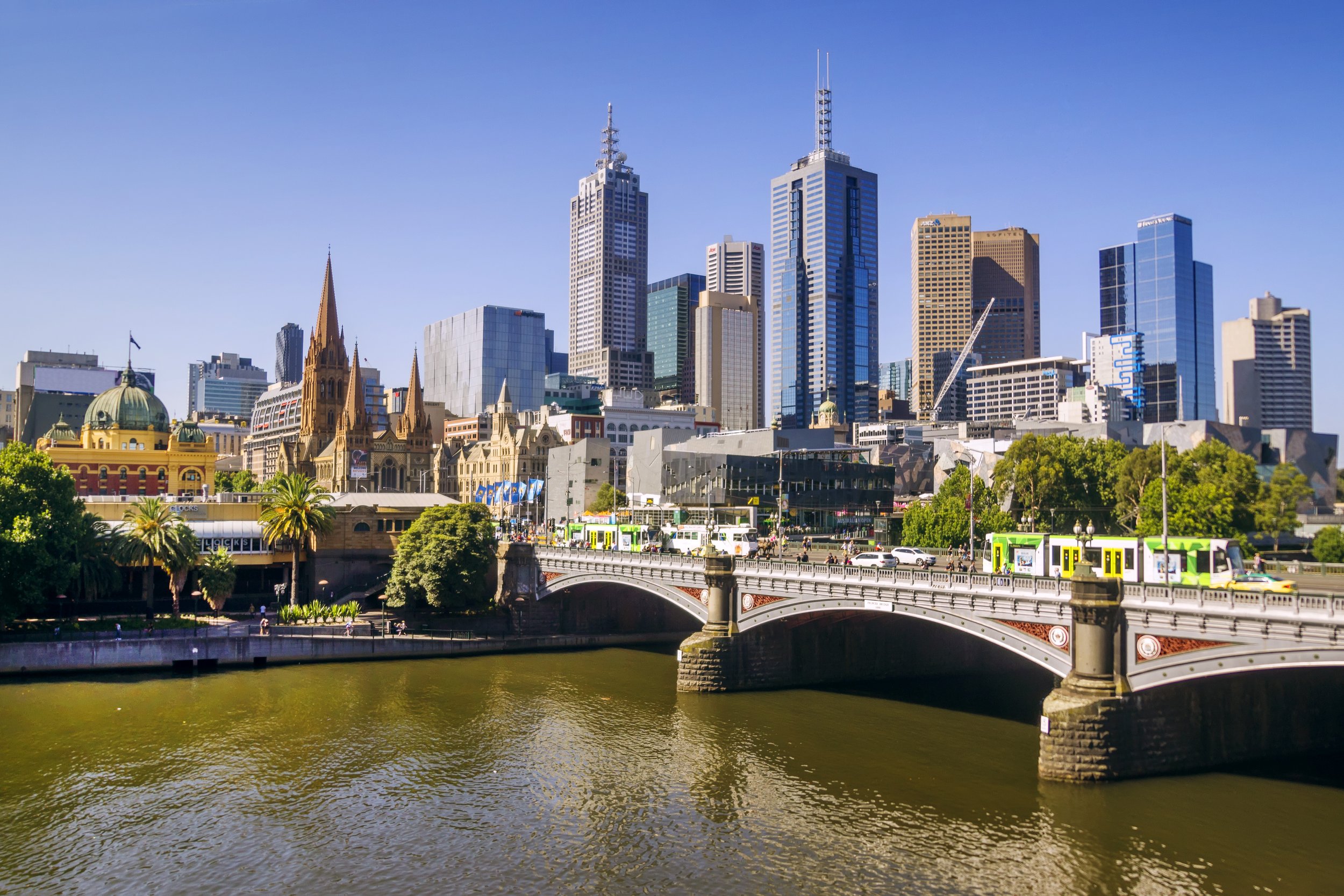 Skyline of a city with tall skyscrapers, historic church, and a bridge over a river in sunny weather.