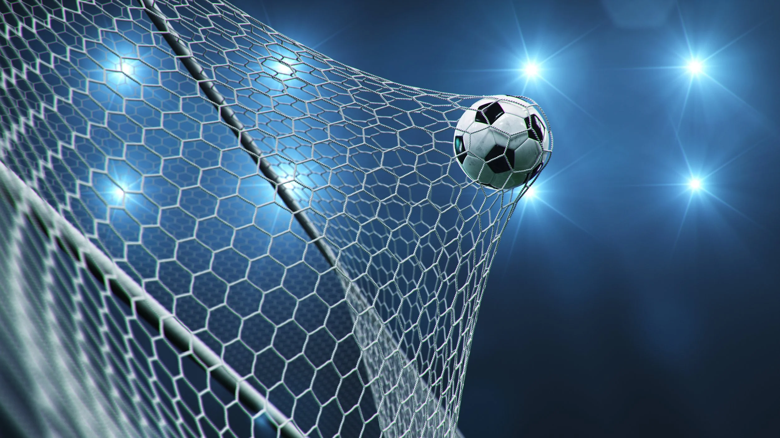 Soccer ball hitting the net in a stadium with bright lights in the background.