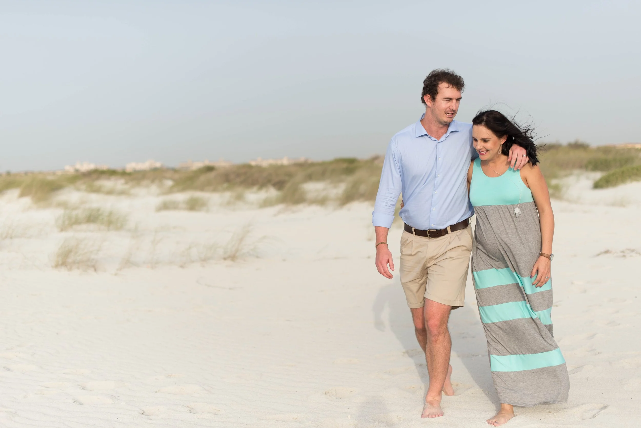 A young man and woman walking barefoot on a sandy beach, smiling and enjoying each other's company.