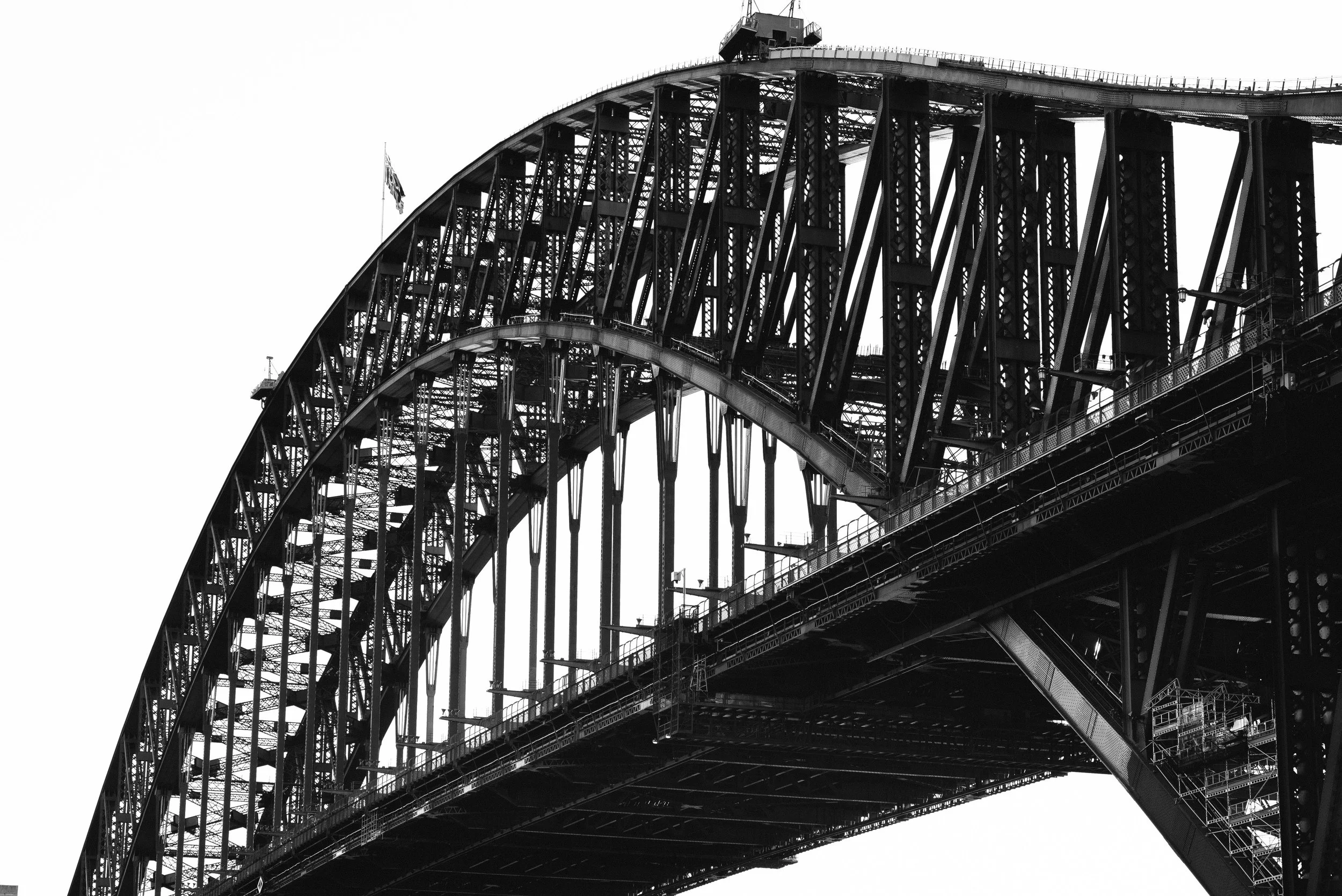 Close-up of the Sydney Harbour Bridge showing its steel arch and structural elements in black and white.
