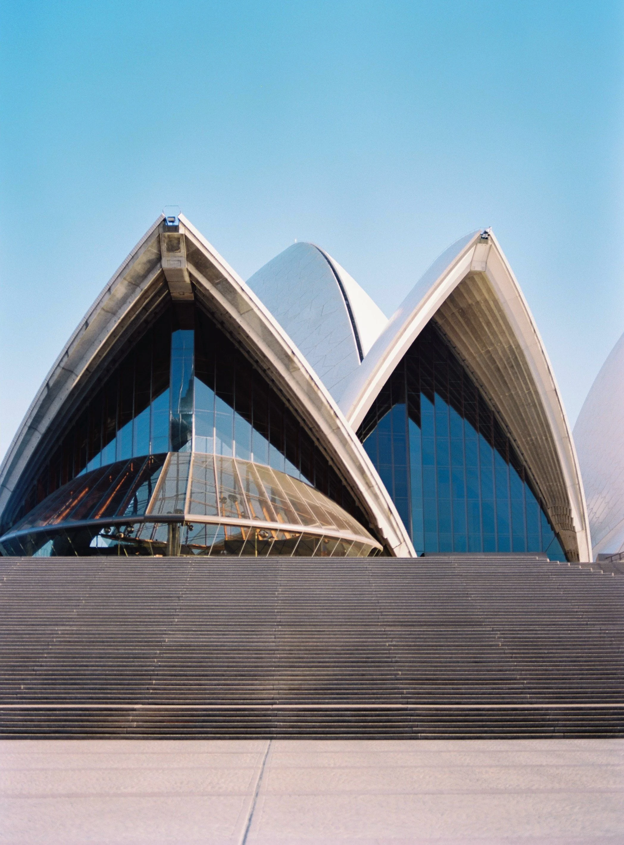 Close-up of the Sydney Opera House with its iconic sail-like white shells against a clear blue sky.
