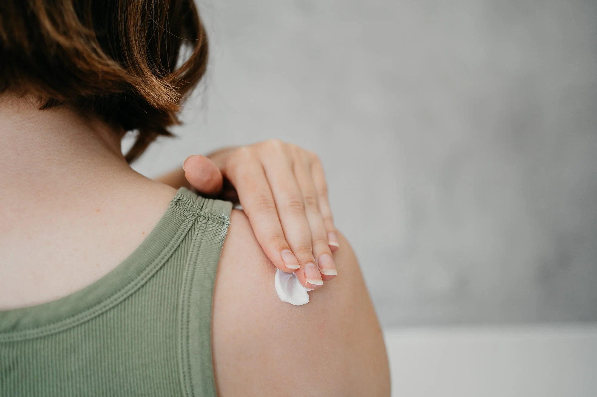 Vrouw die op haar schouder crème aanbrengt.