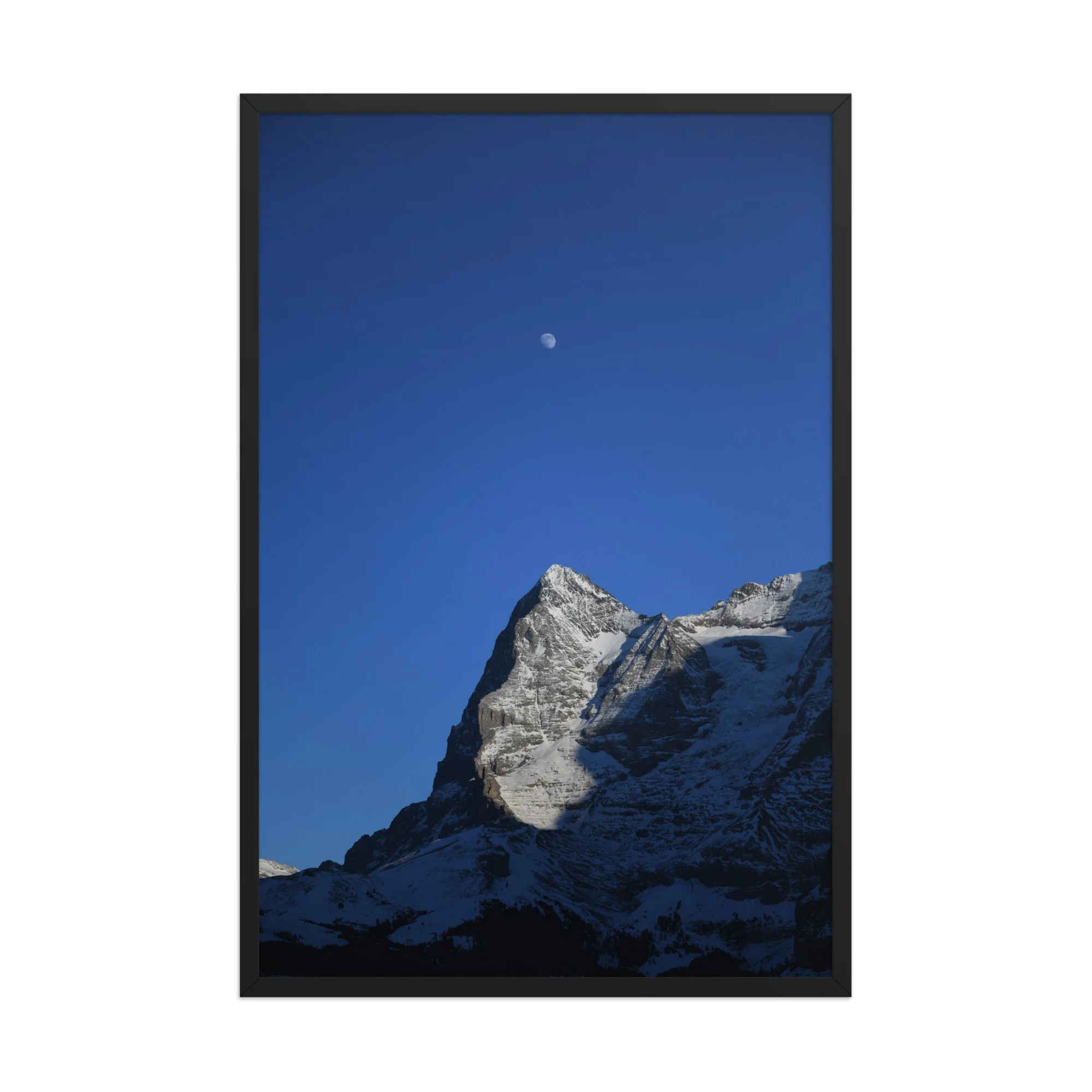 Mond über dem Grat: verschneite Bergkante und Mond im blauen Himmel, Fotografie von Daniel Frei im schwarzen Rahmen. Moon above the ridge, framed photograph.