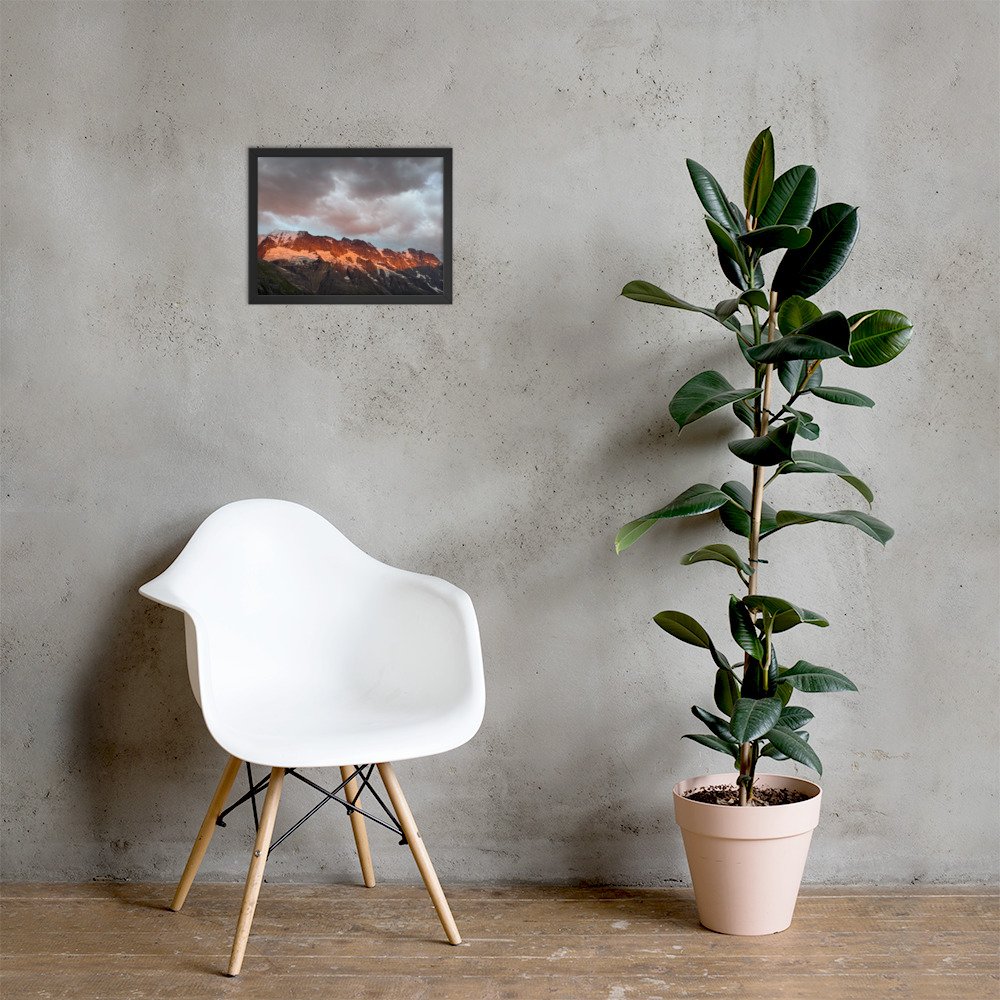 Ein Streifen Wärme: gerahmte Bergfotografie über weissem Stuhl neben einer Pflanze. Raumvisualisierung. A band of warmth: framed mountain photograph above a white chair beside a plant. Room mockup.