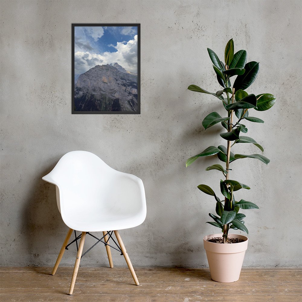 Fels unter offenem Himmel: gerahmte Bergfotografie über weissem Stuhl neben einer Pflanze. Raumvisualisierung. Framed mountain photograph above a white chair beside a plant. Room mockup.