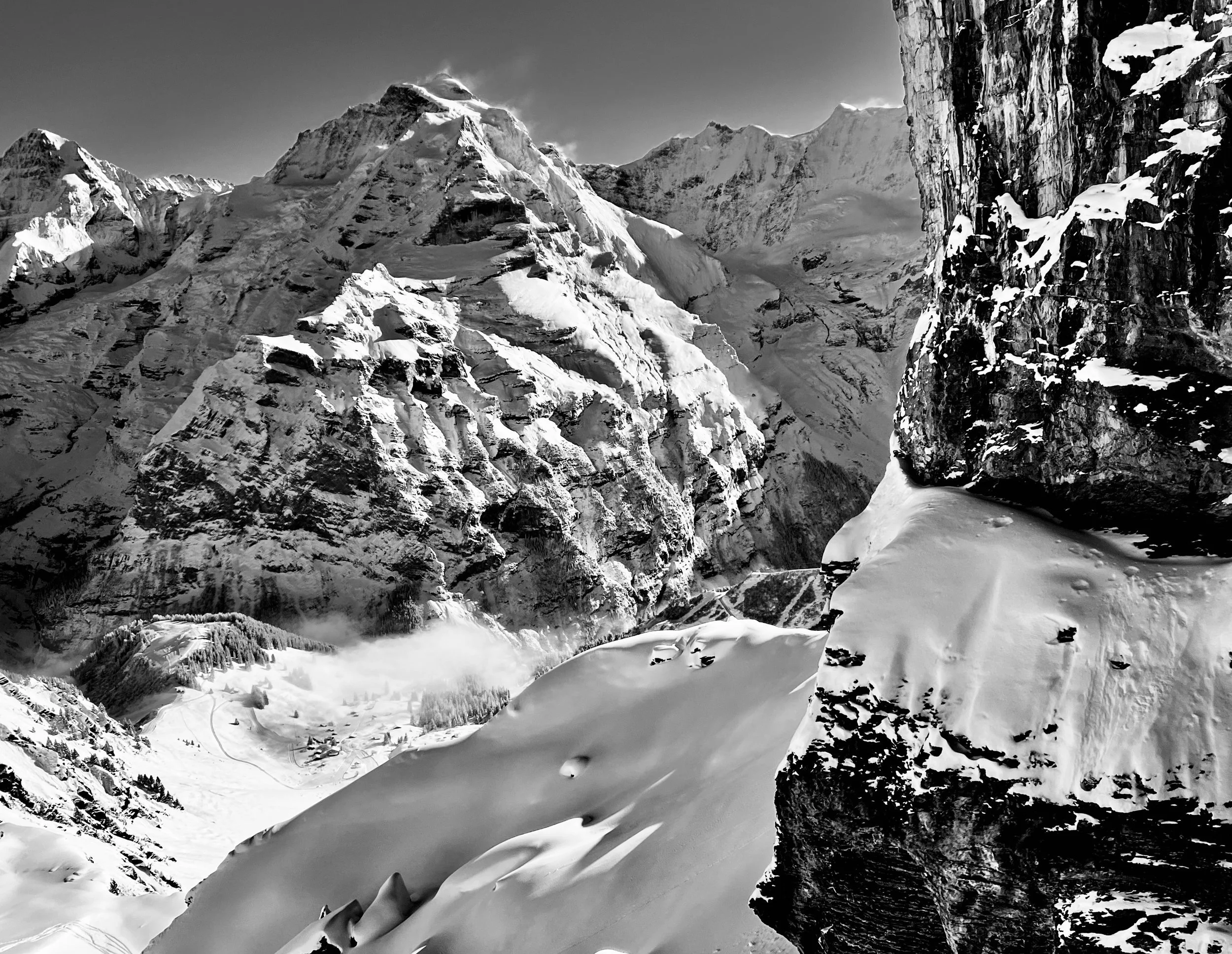 Schneehänge und Felswand im Vordergrund einer Berglandschaft in Schwarzweiss.