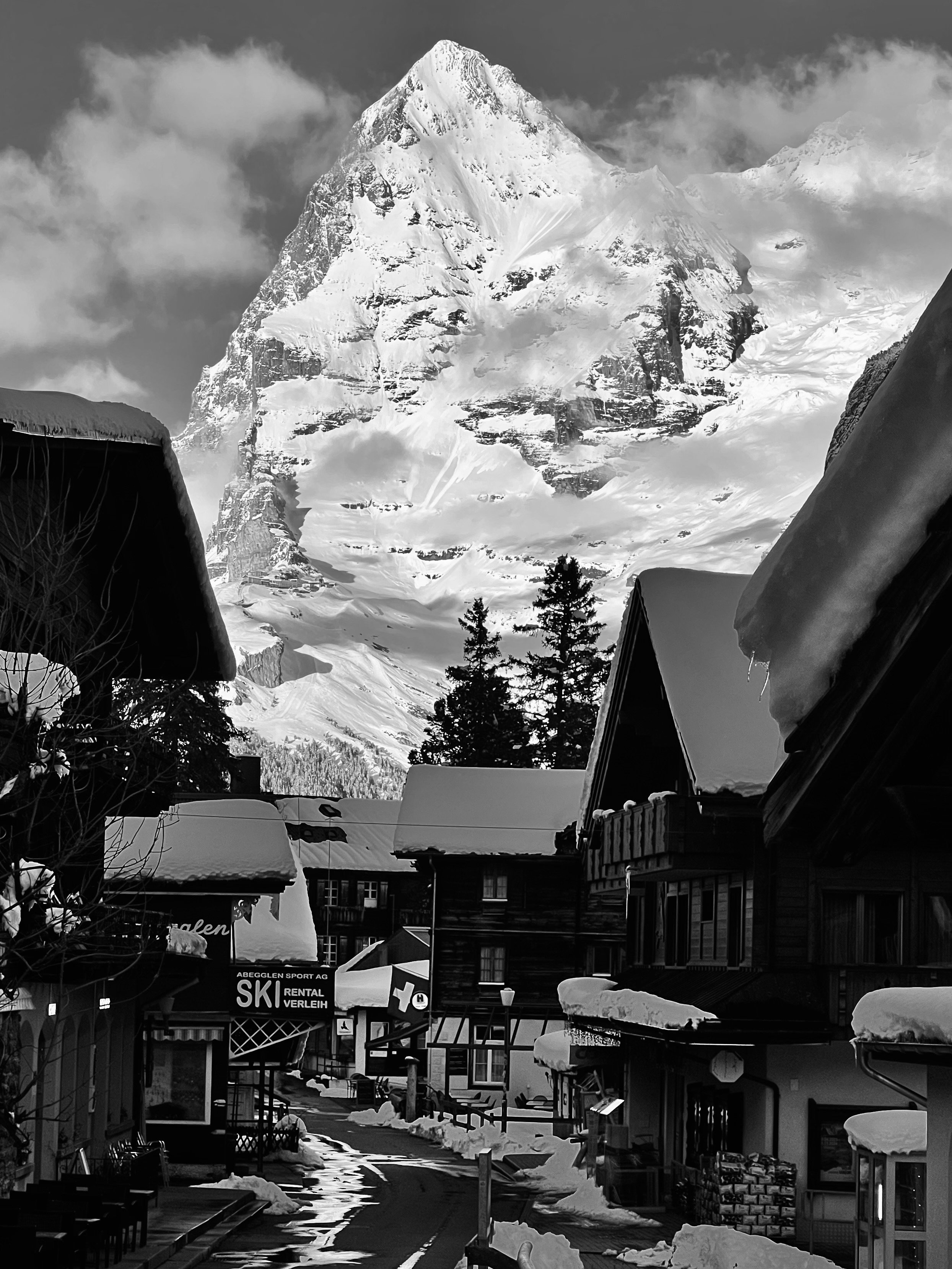 Blick zwischen Häusern auf einen verschneiten Berg in Schwarzweiss.