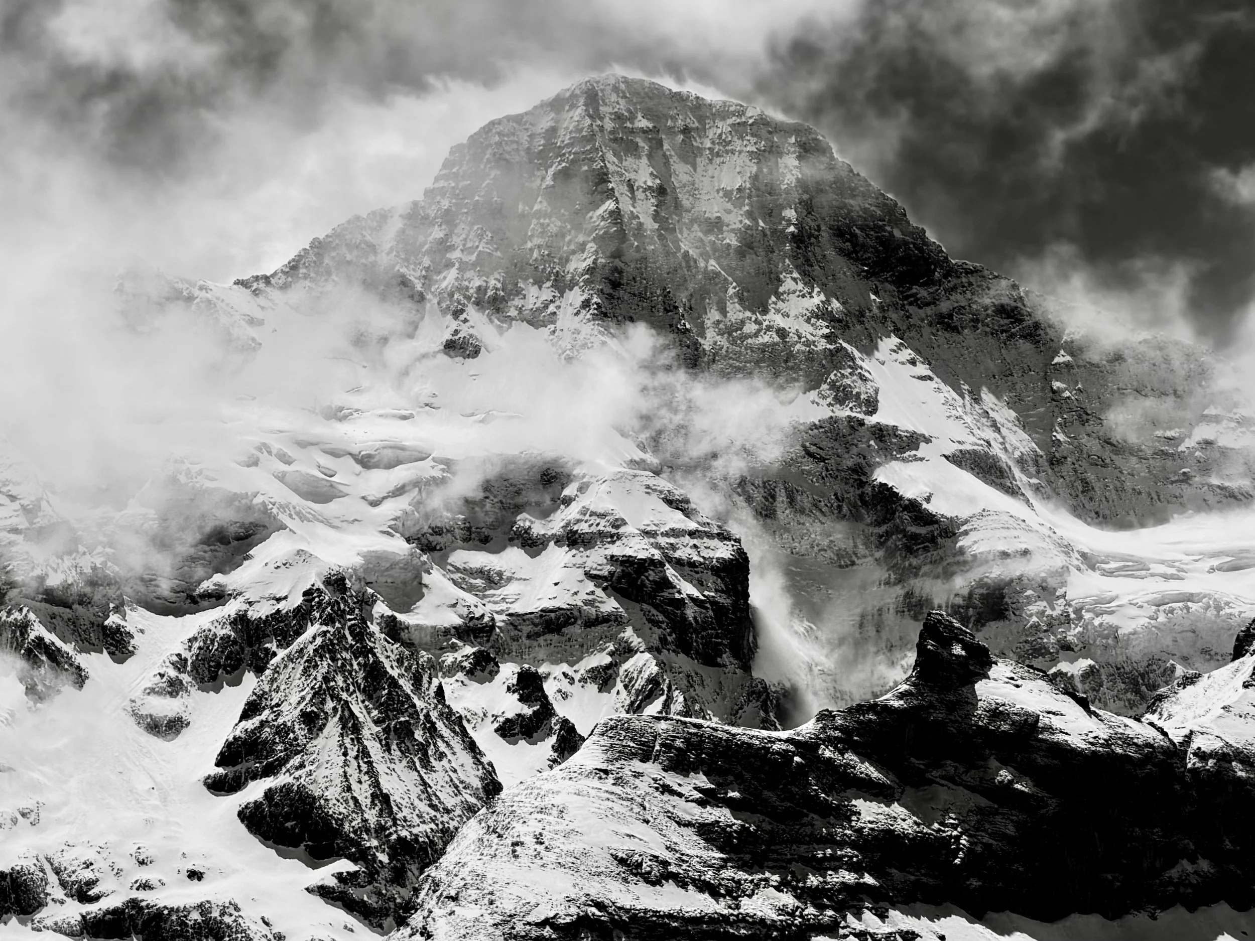 Massiver verschneiter Berg zwischen Wolken in Schwarzweiss.