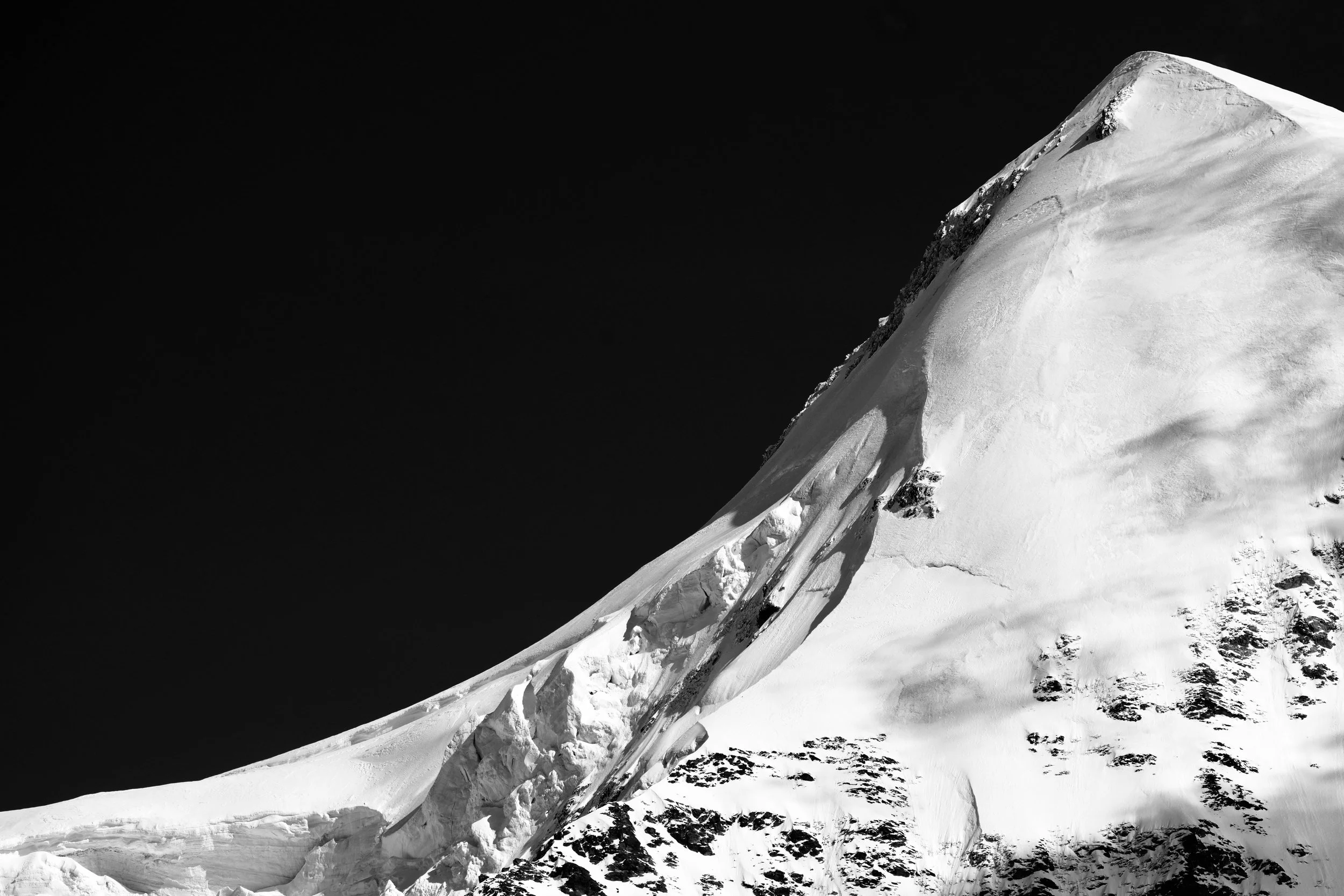 Helle Schneeflanke mit einer ansteigenden Gratlinie vor dunklem Himmel.