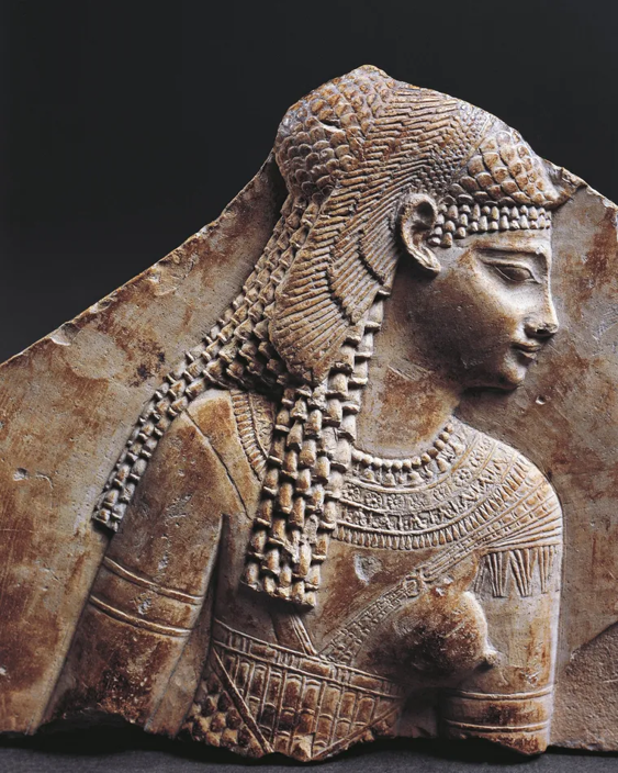 Relief en pierre représentant une femme égyptienne antique avec une coiffe et des bijoux détaillés.