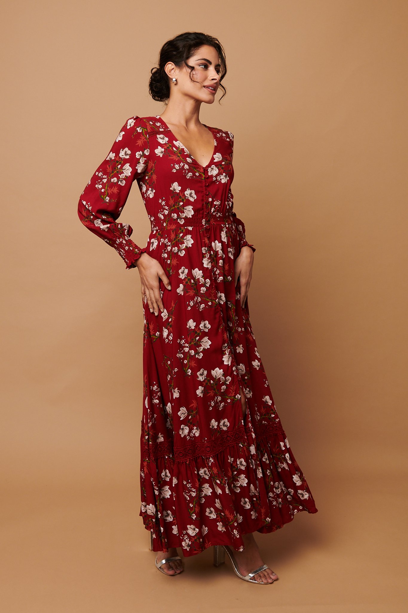 A woman in a long red floral dress with puffed sleeves and a v-neckline, standing against a beige background.