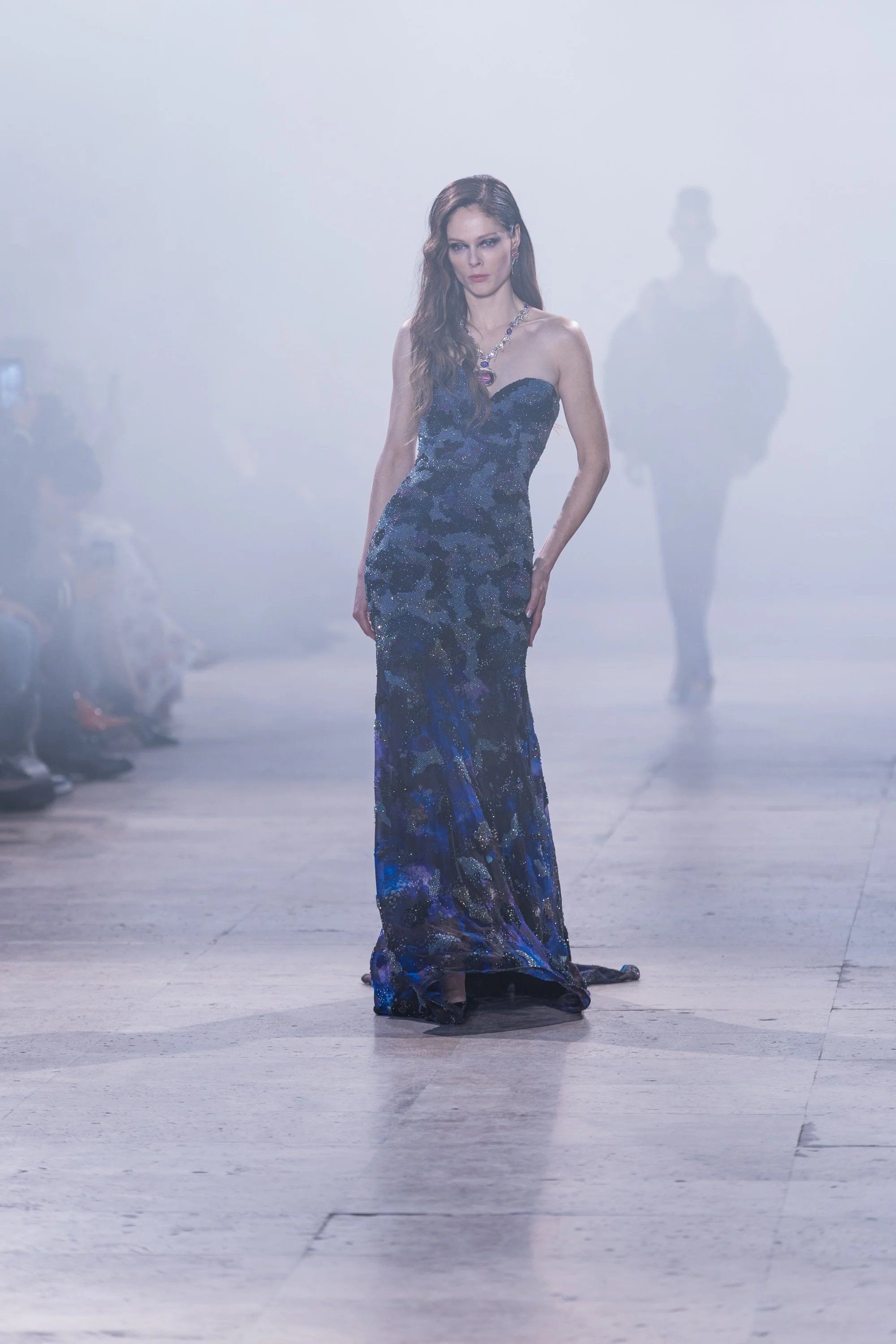Model walking on a runway wearing an avant-garde gown with large, sculptural, wave-like fabric elements and high slit, in a fashion show setting for gaurav gupta paris haute couture week. Gaurav Gupta is Indian fashion designer.