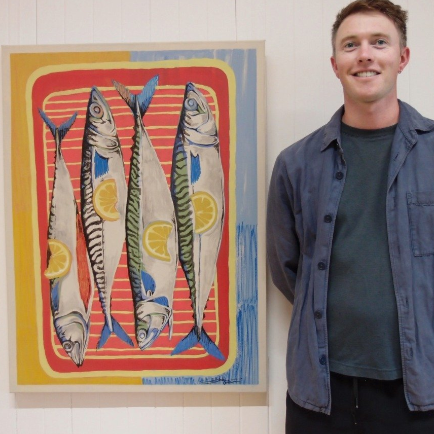 A man standing beside a colorful painting of four fish with lemon slices, set against a vibrant background with red, yellow, and blue hues.