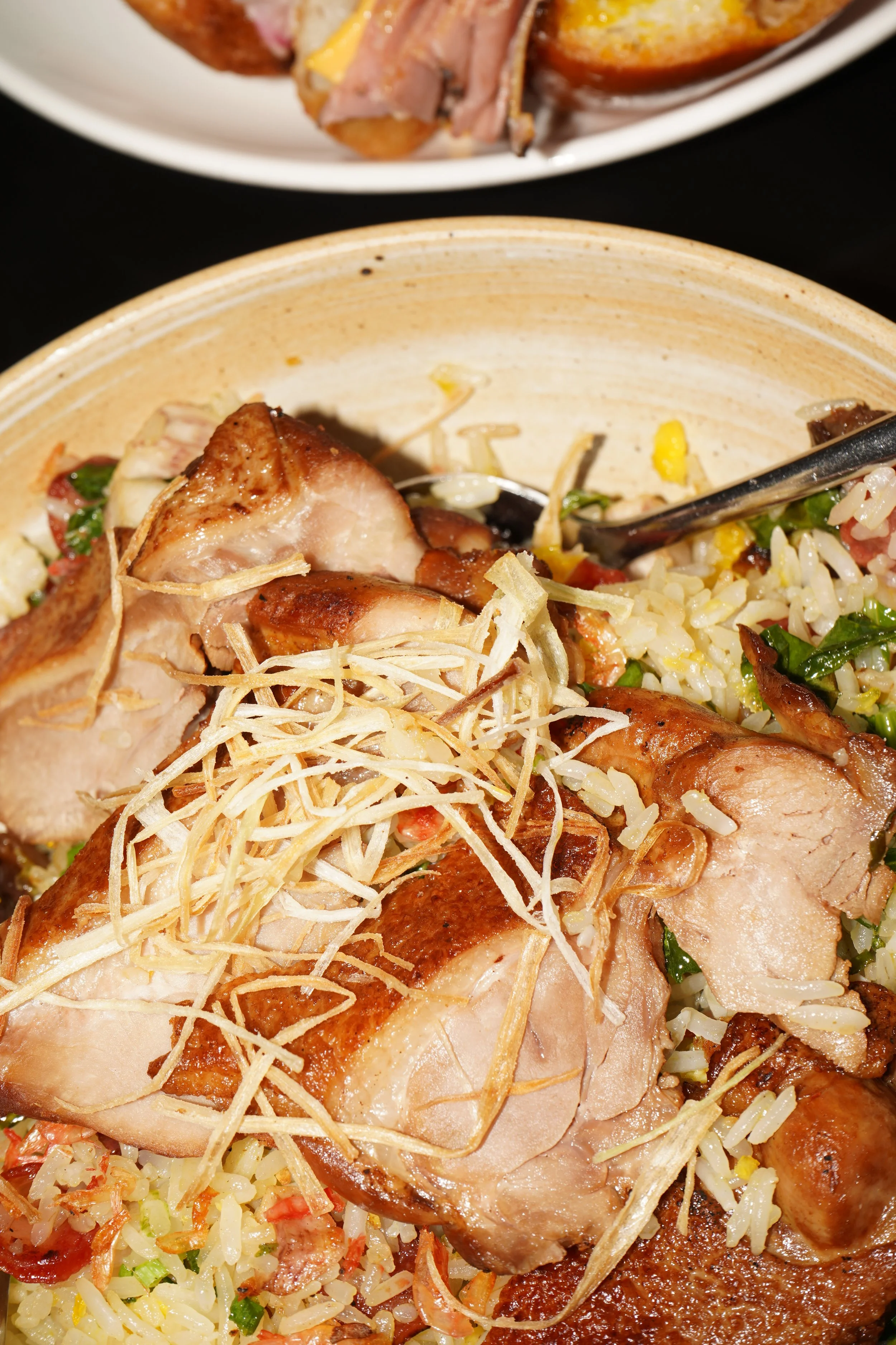 Close-up of roasted chicken served over rice and vegetables with shredded ginger on top.