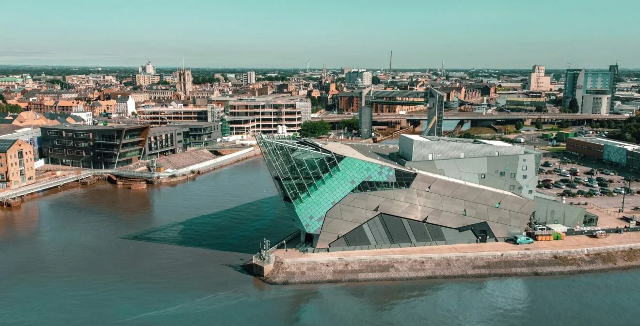 Aerial view of a city waterfront featuring modern architectural buildings, including a large angular glass structure.