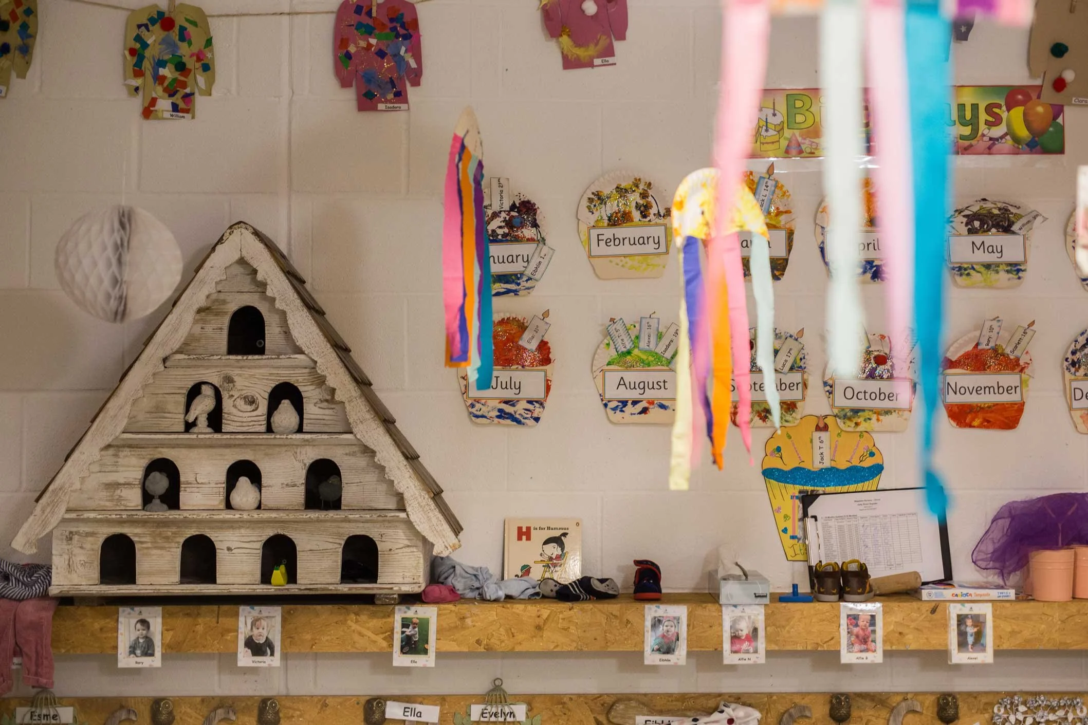 Classroom decorated with colorful paper craft projects of umbrellas and cupcake cutouts on a wall, with labeled months of the year.