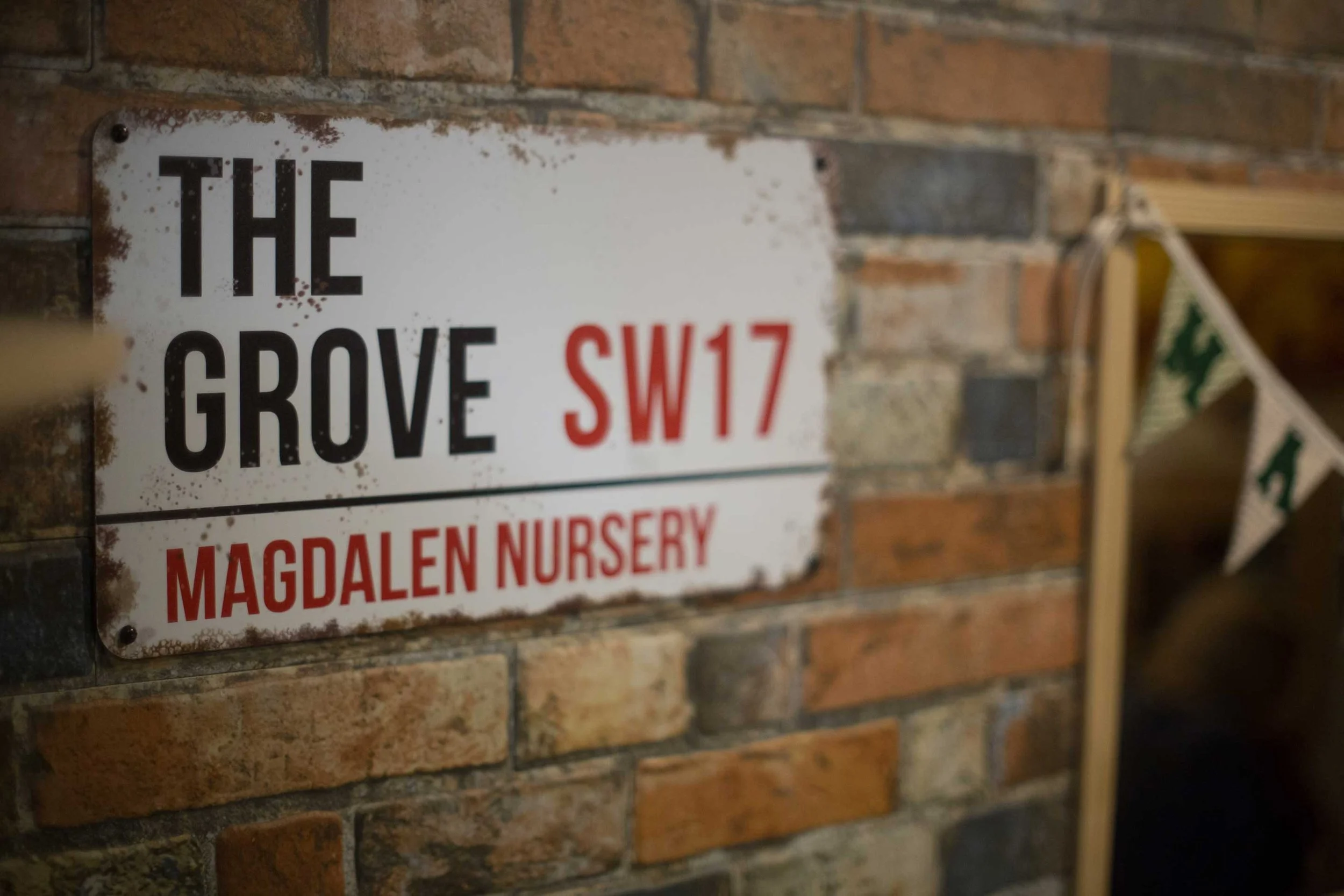 Artificial street sign on an artificial brick wall reading 'The Grove SW17  Magdalen Nursery'.