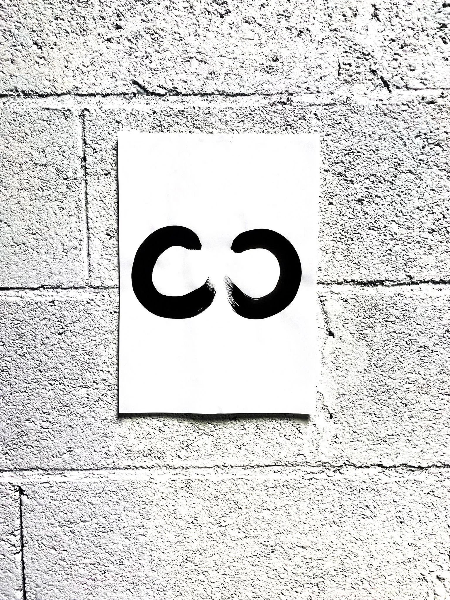 Affiche avec deux formes circulaires noires sur un mur en briques grises.