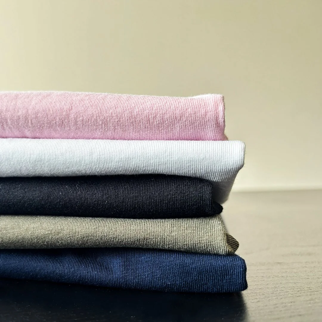 Stack of folded colorful t-shirts, including pink, white, black, beige, and navy, on a wooden surface.