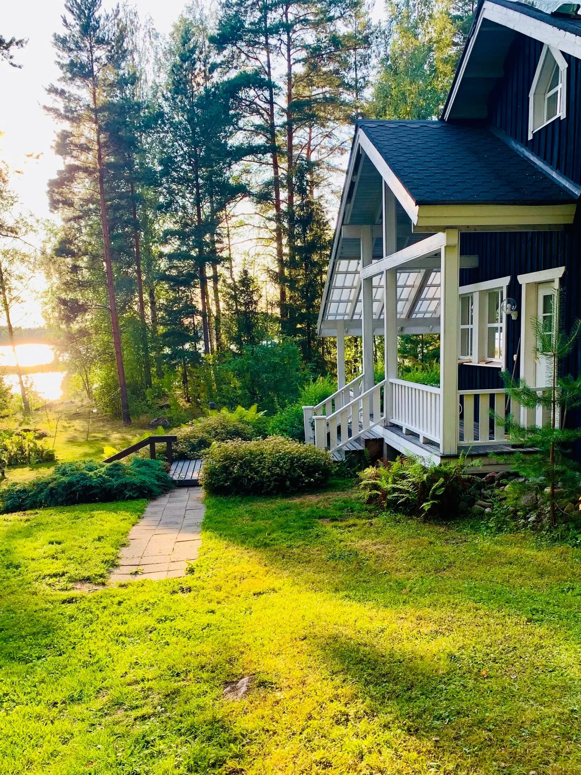 Blue wooden lakeside villa with terrace overlooking Lake Saimaa on a sunny summer day, surrounded by Finnish nature and peaceful scenery.