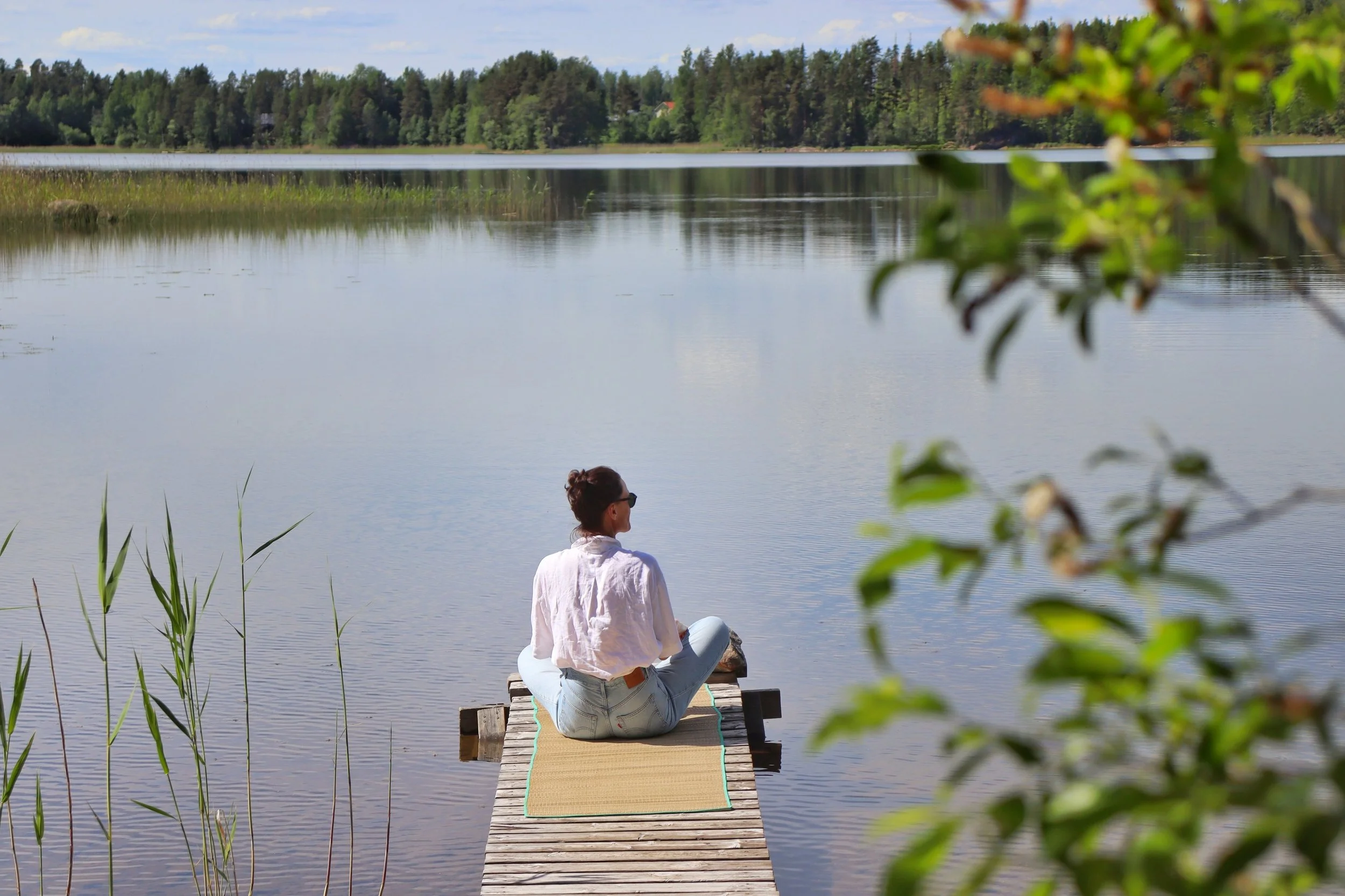A woman sits alone at the end of the wooden pier at Blueberry Villa, gazing across the calm waters of Lake Saimaa. Surrounded by the quiet beauty of the Finnish Lakeland, she enjoys a peaceful moment of reflection and connection with nature.