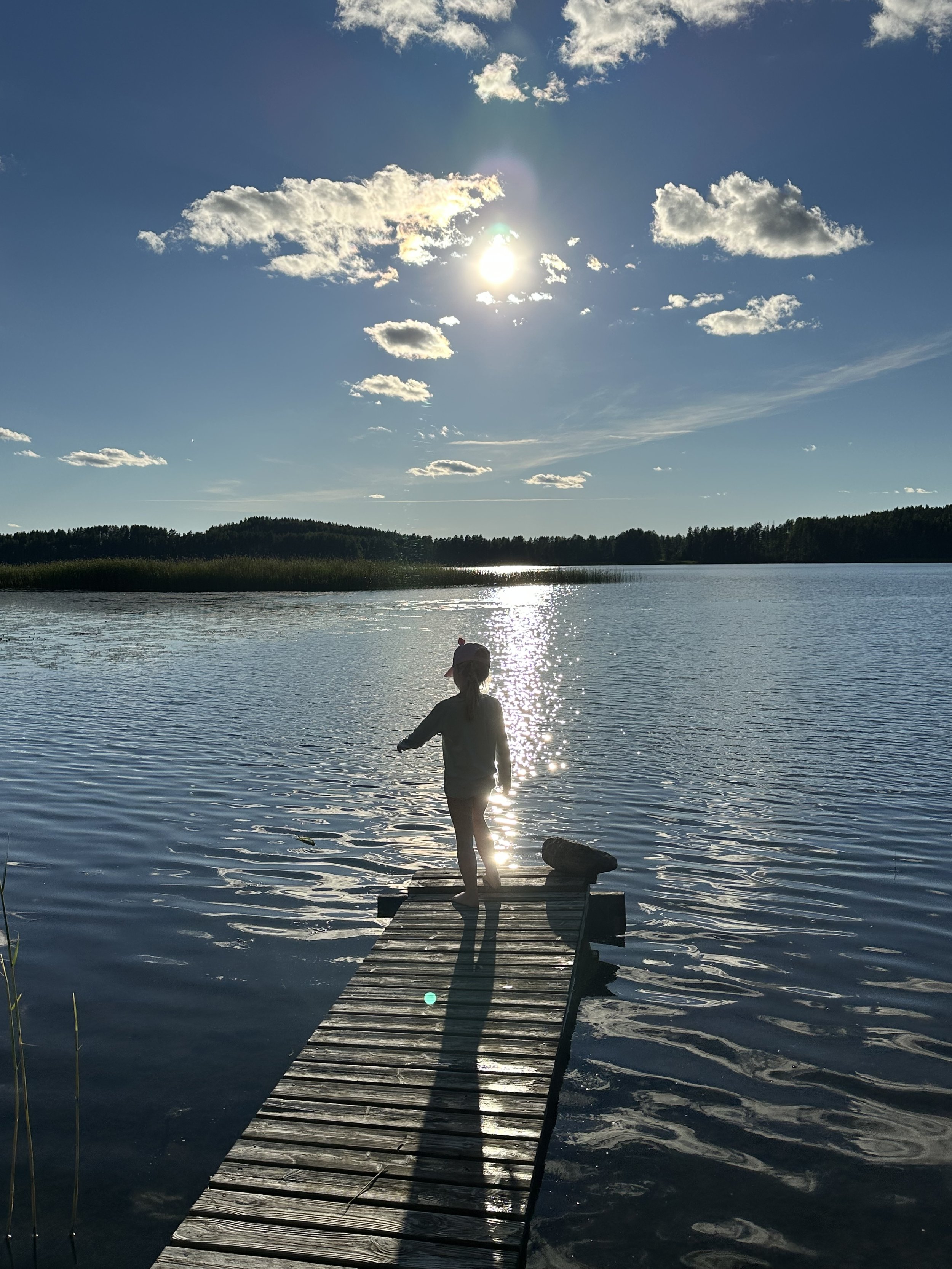 A small child stands on the wooden pier at Blueberry Villa during a golden Lake Saimaa sunset. The calm, shallow shoreline provides a safe place for children to play, swim, and explore the water while enjoying the peaceful beauty of the Lakeland.