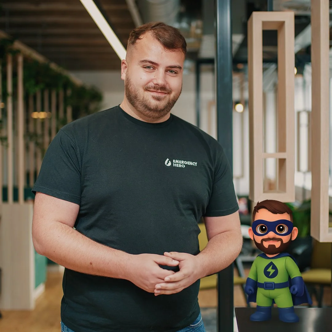 3D animated character of a man with brown hair, a beard, wearing a black T-shirt, standing in front of a dark background with the text 'EMERGENCY HERO' and a water droplet logo with a lightning bolt.