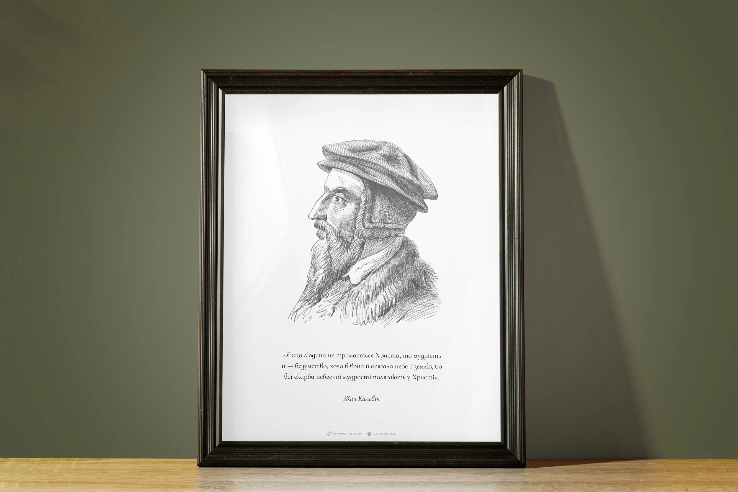 Schwarz-weiß Zeichnung eines Mannes im Profilrahmen, Text darunter auf Ukrainisch, auf Holztisch vor grünem Hintergrund.