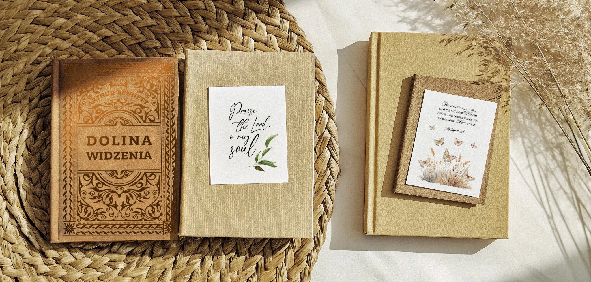 Zwei Bücher auf einem Geflechtuntergrund, eines davon mit der Aufschrift 'Dolina Widzenia'. Auf den Büchern liegen Karten mit religiösen Zitaten und botanischen Illustrationen.