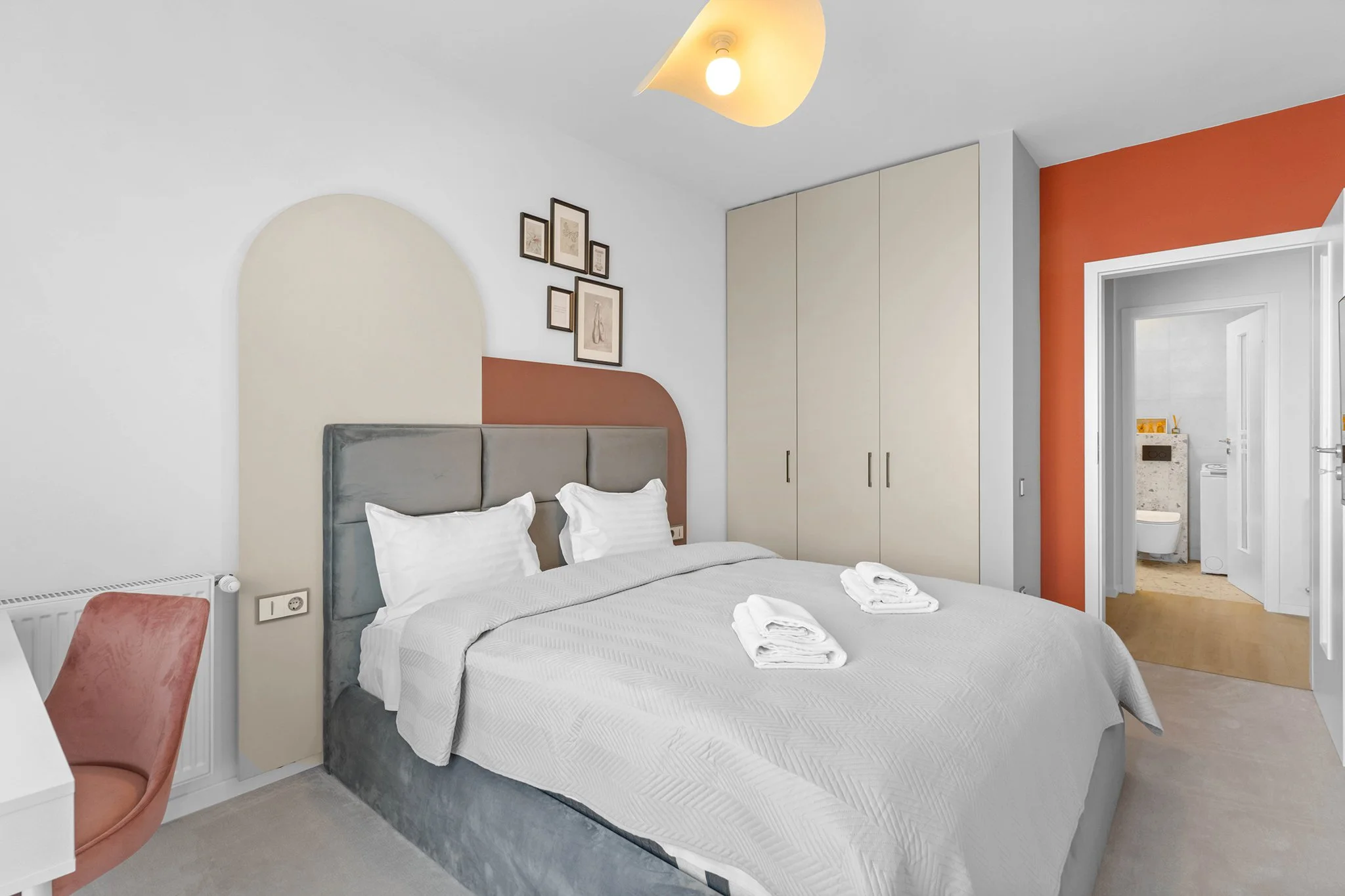 Modern bedroom with double bed, minimalist decor, framed art above headboard, closet, and view into bathroom.