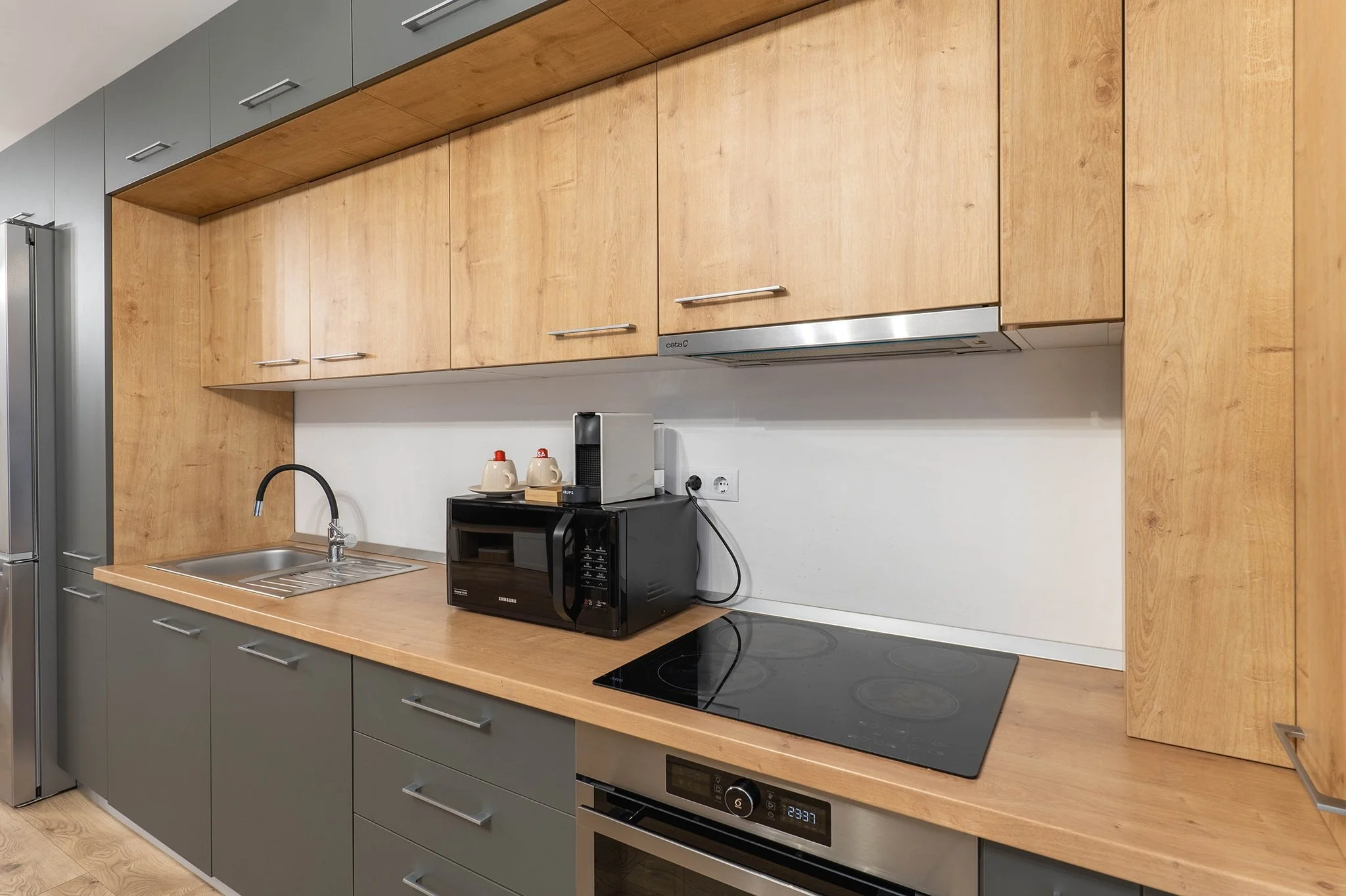 Modern kitchen with wooden cabinets, stainless steel sink, electric cooktop, built-in oven, microwave, and coffee machine on the counter.